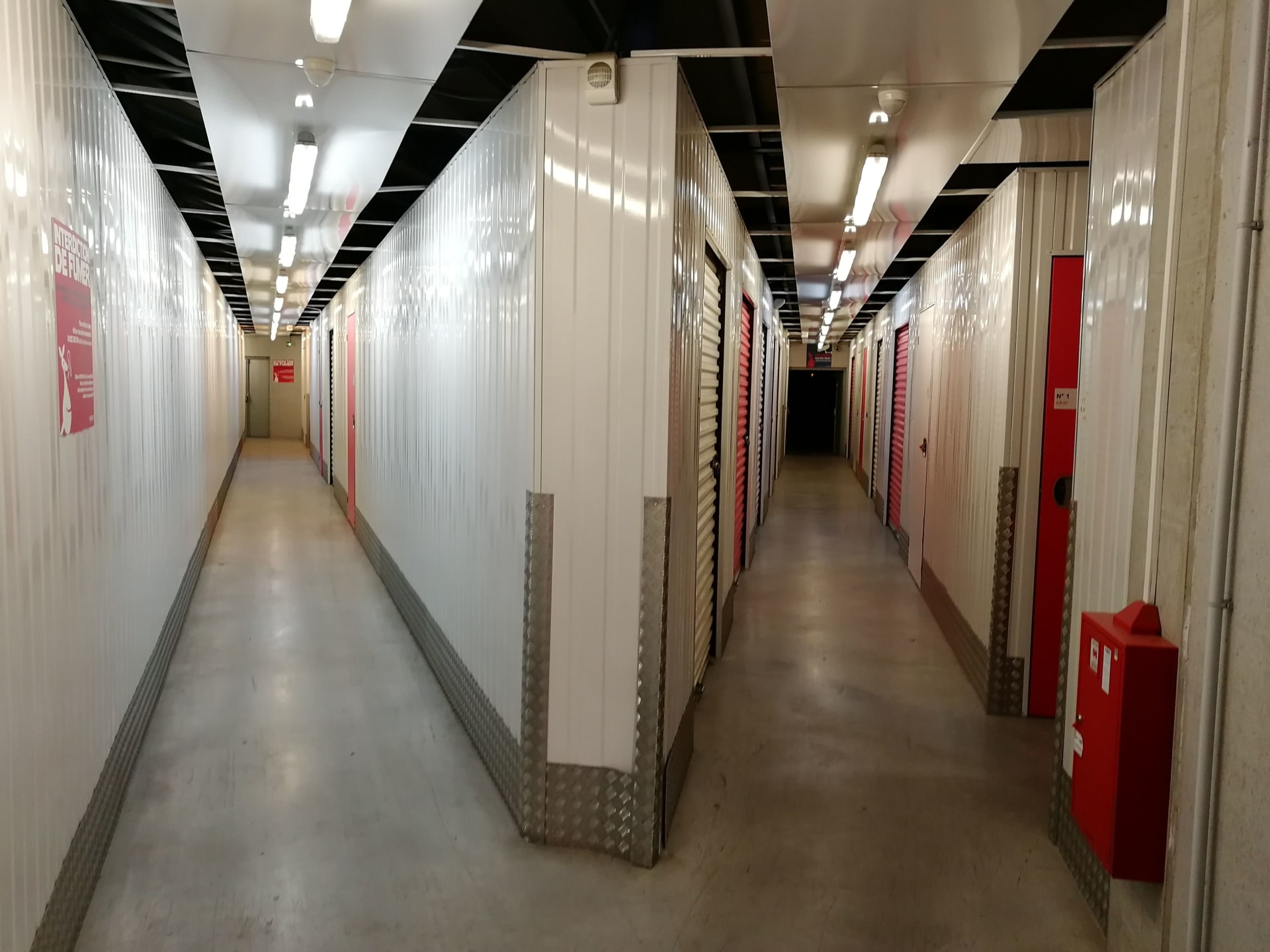 Couloir intérieur avec portes de boxes blanches et rouges et extincteur du centre HOMEBOX Paris Ternes