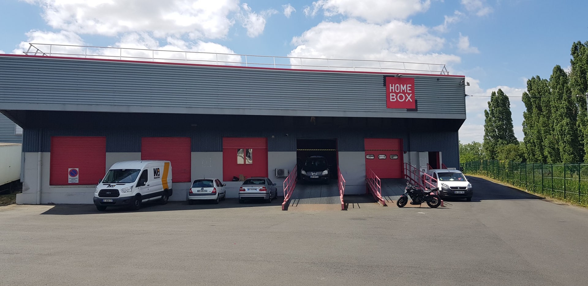 Façade avec enseigne et quais de chargement avec véhicules clients, HOMEBOX Longjumeau, 6 rue du Canal à Longjumeau