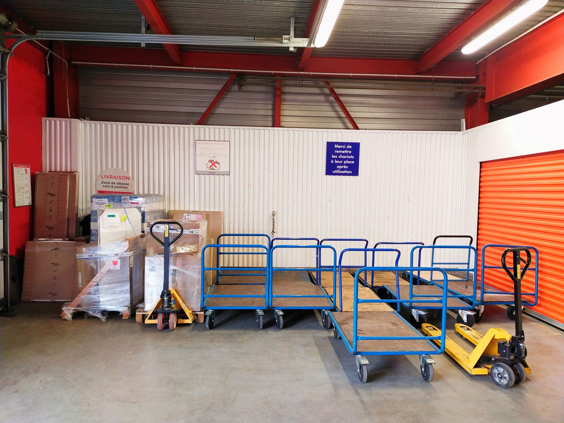 Zone de livraison intérieure avec chariots bleus, transpalettes et cartons stockés du centre HOMEBOX Maurepas