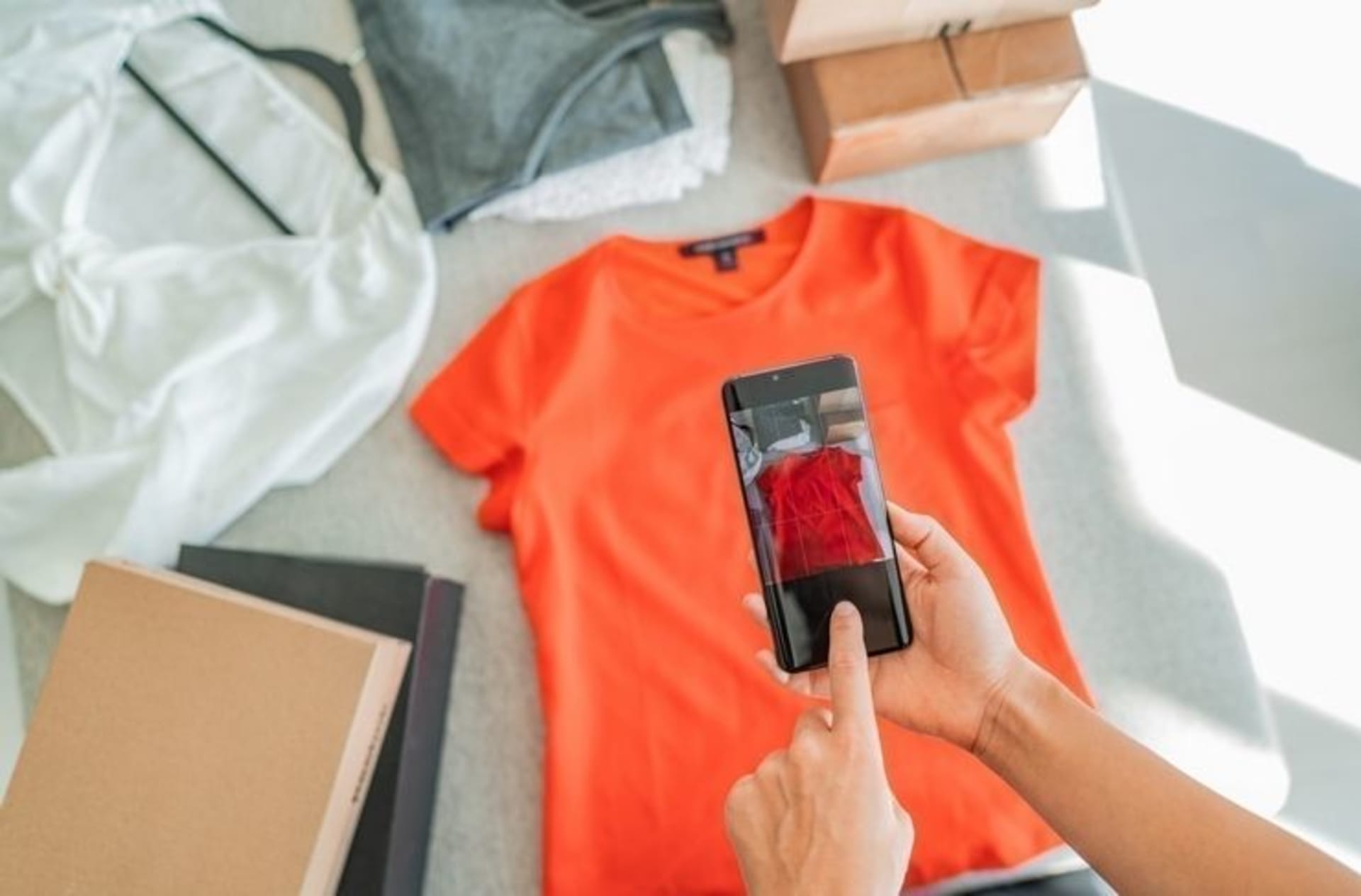 Mains photographiant un t-shirt orange avec un smartphone pour le mettre en don en ligne