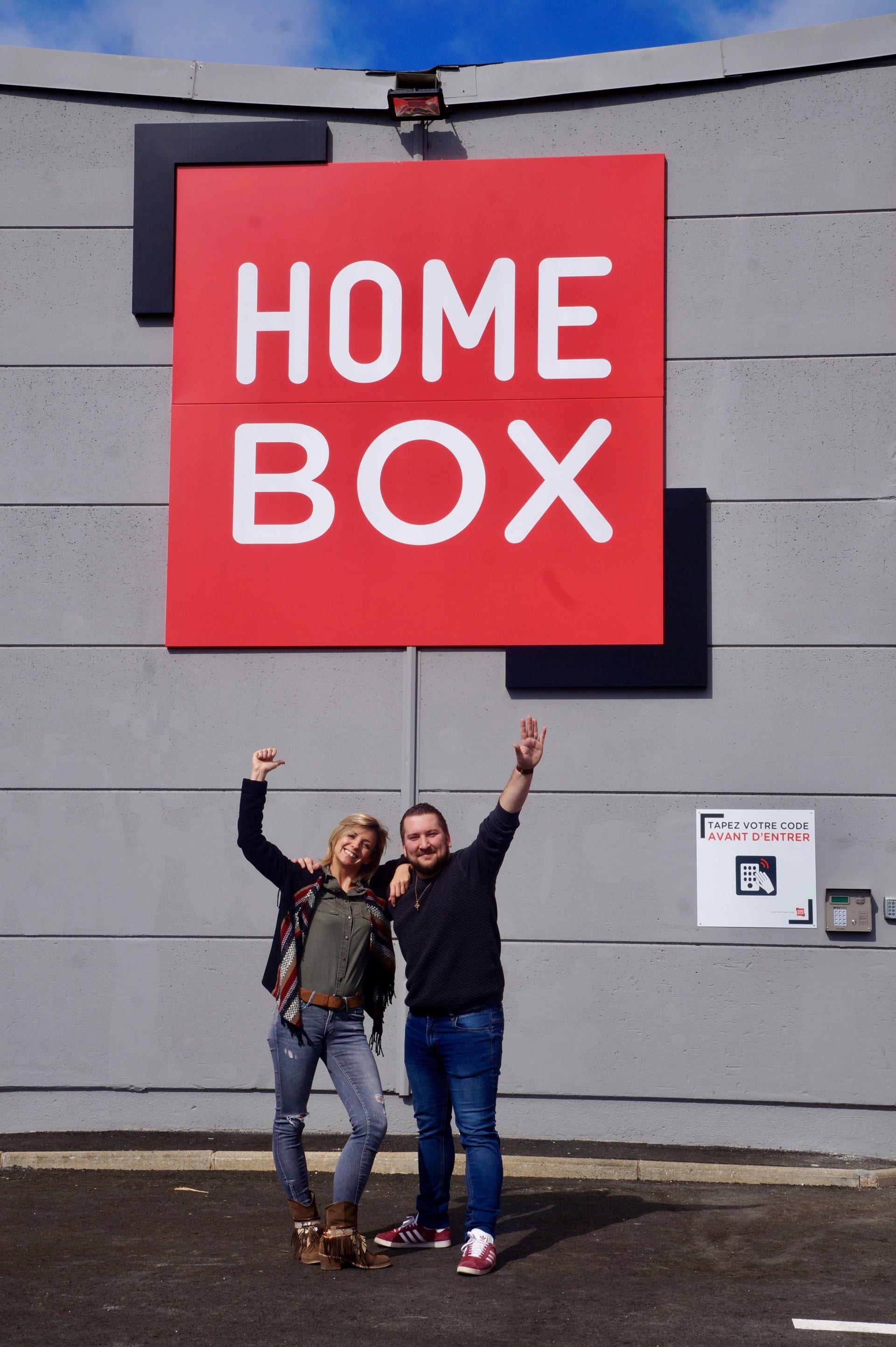 Couple souriant bras levés devant le logo rouge HOMEBOX, HOMEBOX Montpellier, 925 Avenue du Marché Gare à Montpellier