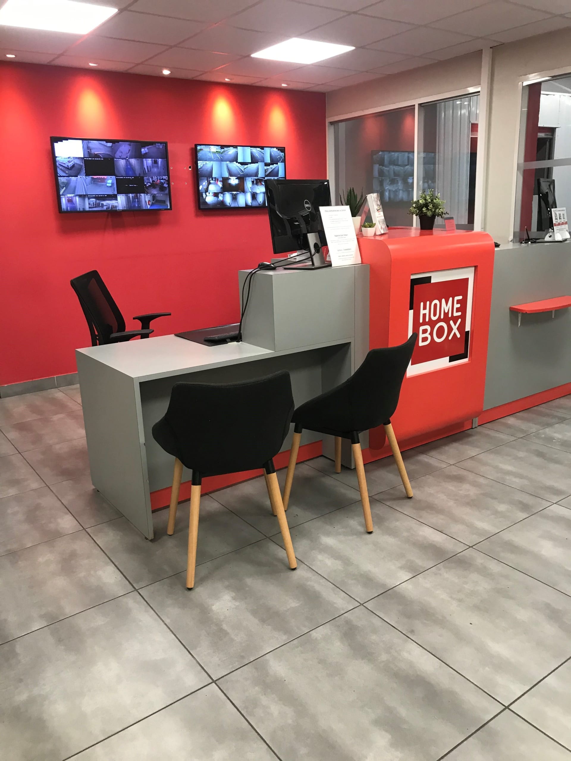 Comptoir d'accueil rouge avec écrans de surveillance et coin réception du centre HOMEBOX Montpellier