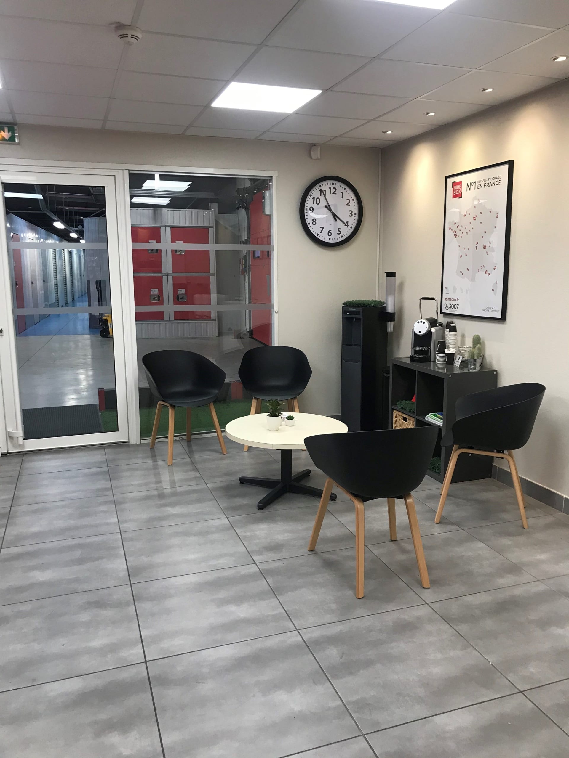 Salon d'attente avec fauteuils noirs, horloge et carte des centres du centre HOMEBOX Montpellier