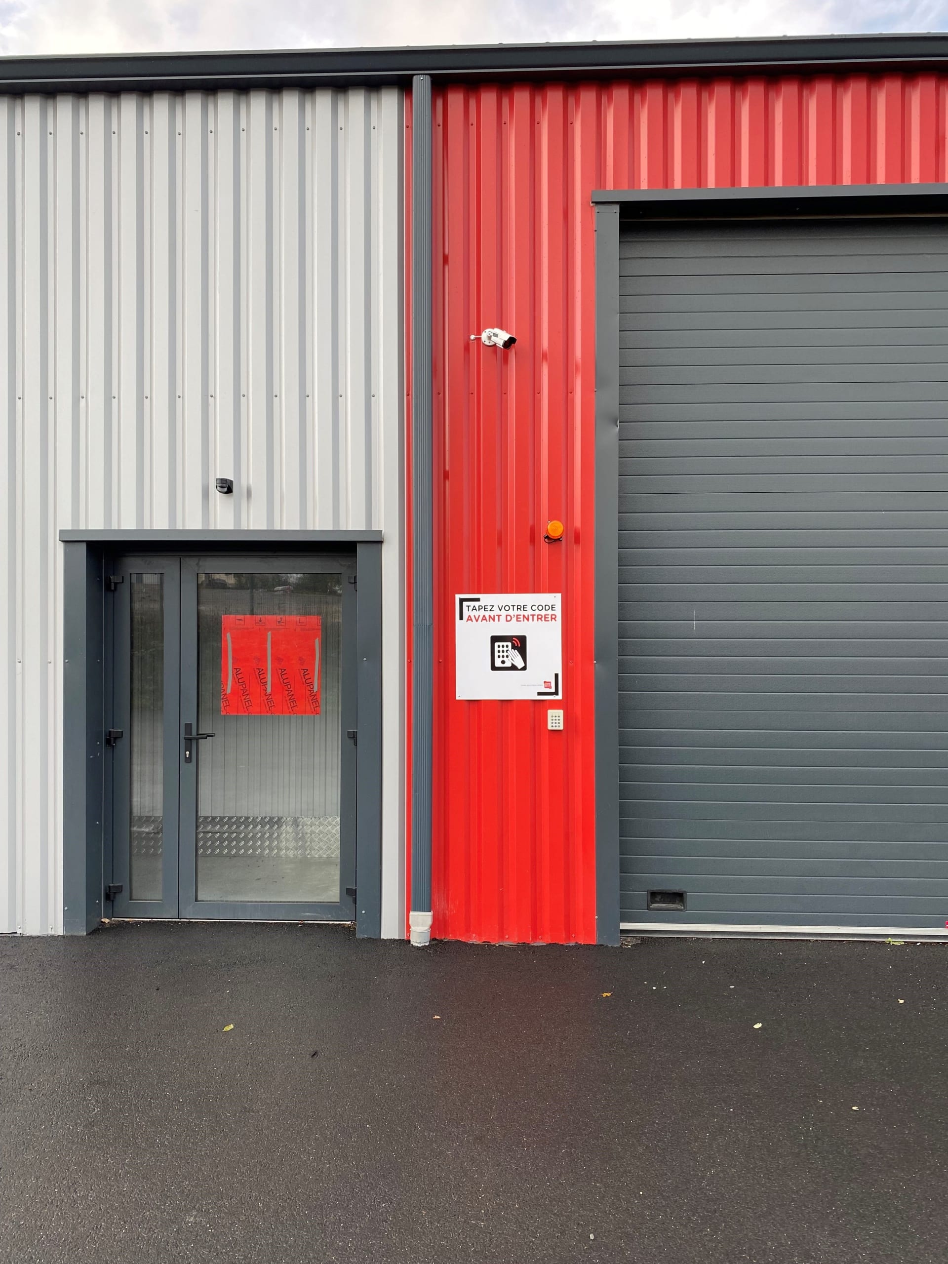 Entrée du centre HOMEBOX Bressuire avec porte vitrée et porte roulante grise.