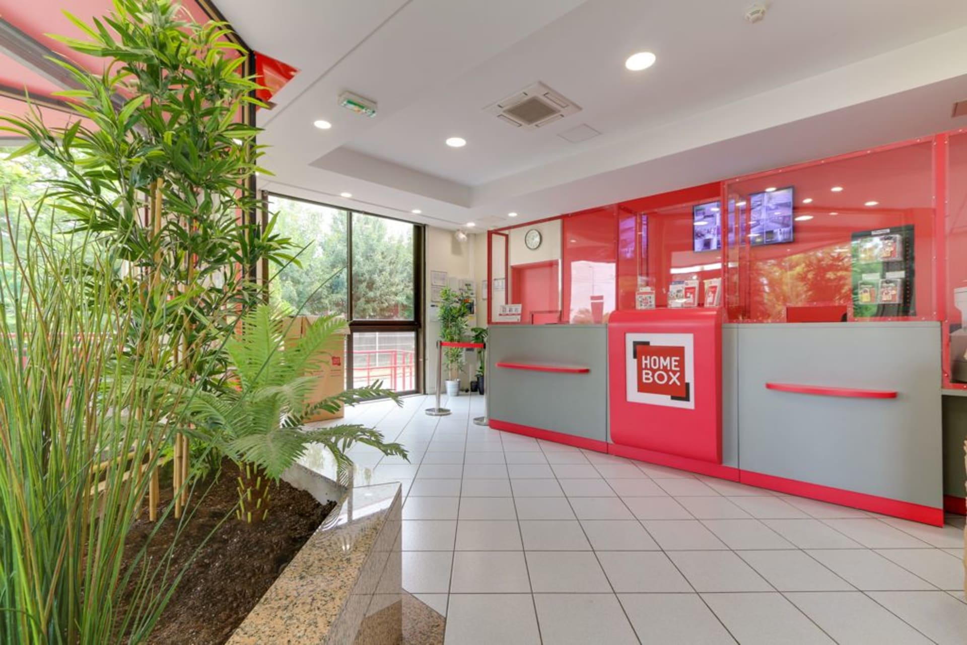 Comptoir d'accueil rouge et gris avec plantes vertes et baie vitrée du centre HOMEBOX Boissy-Saint-Léger