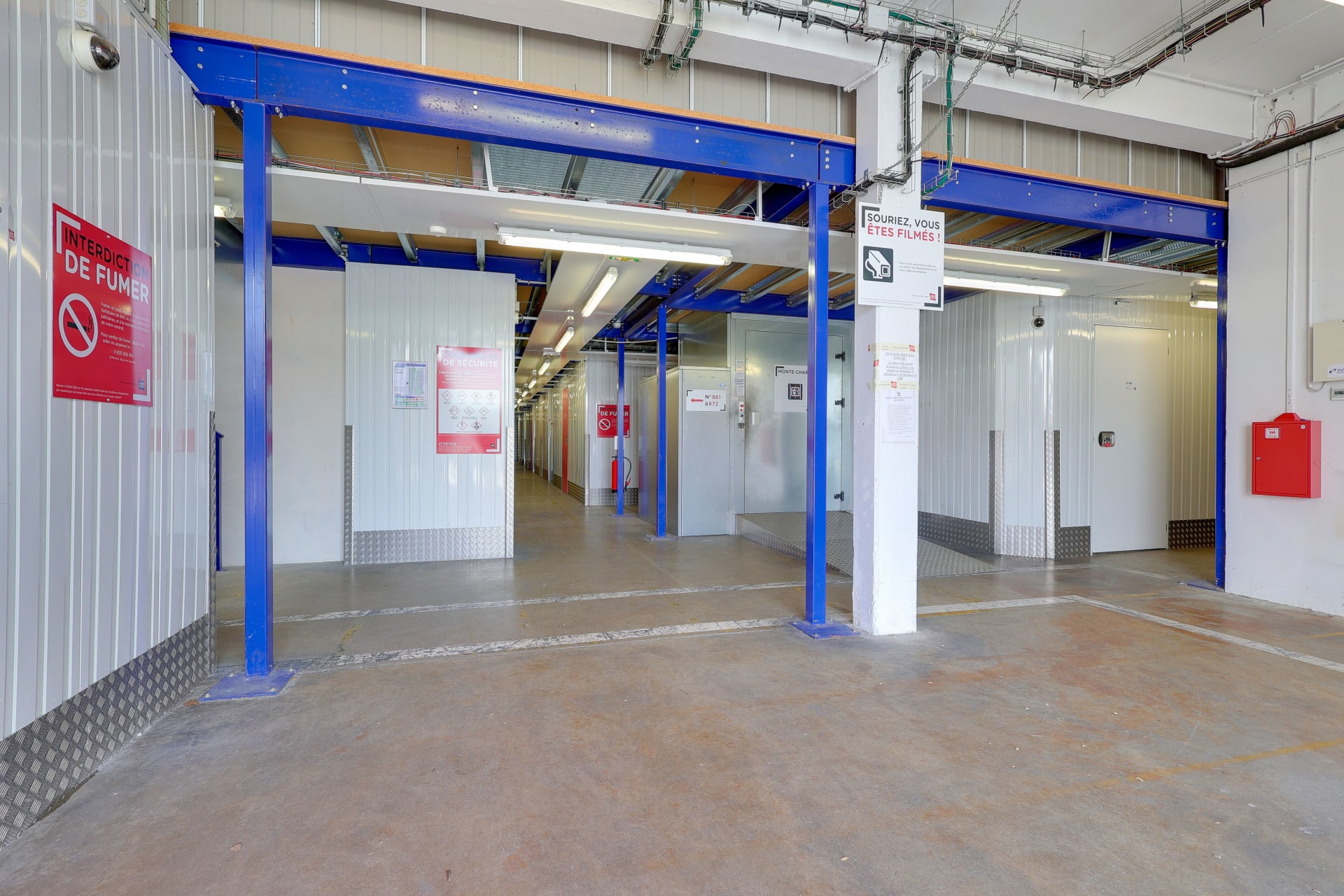 Hall intérieur avec poutres bleues, signalétique et accès aux différentes allées de boxes du centre HOMEBOX Toulouse Fondeyre