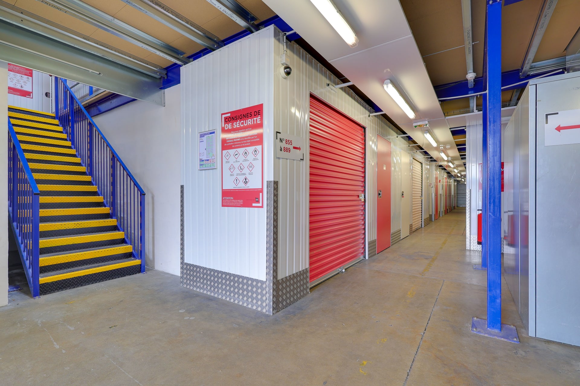 Espace avec escalier métallique bleu et jaune menant à l'étage des boxes du centre HOMEBOX Toulouse Fondeyre