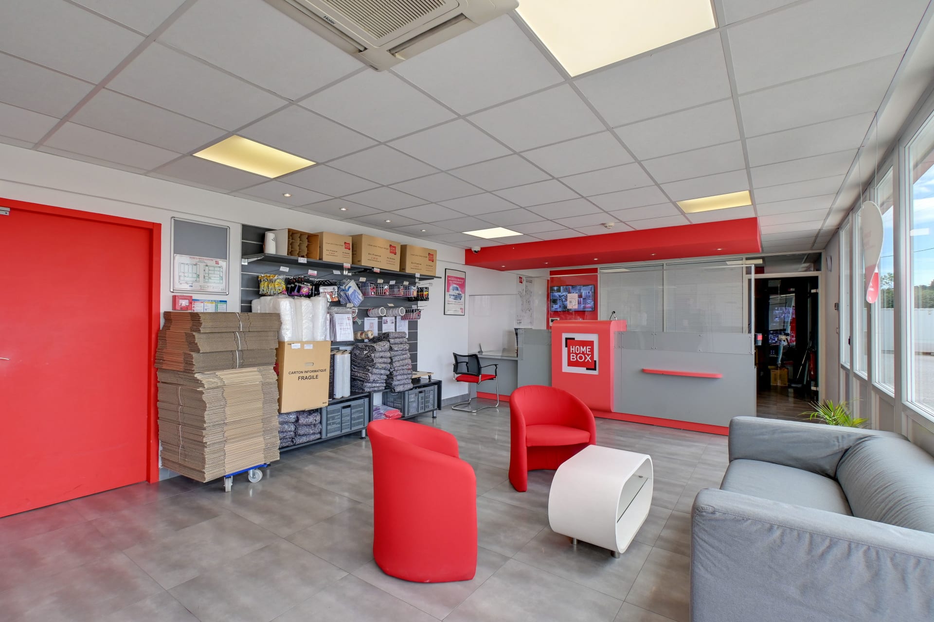 Espace d'accueil lumineux avec fauteuils rouges, comptoir et présentoir de cartons du centre HOMEBOX Les Pennes-Mirabeau
