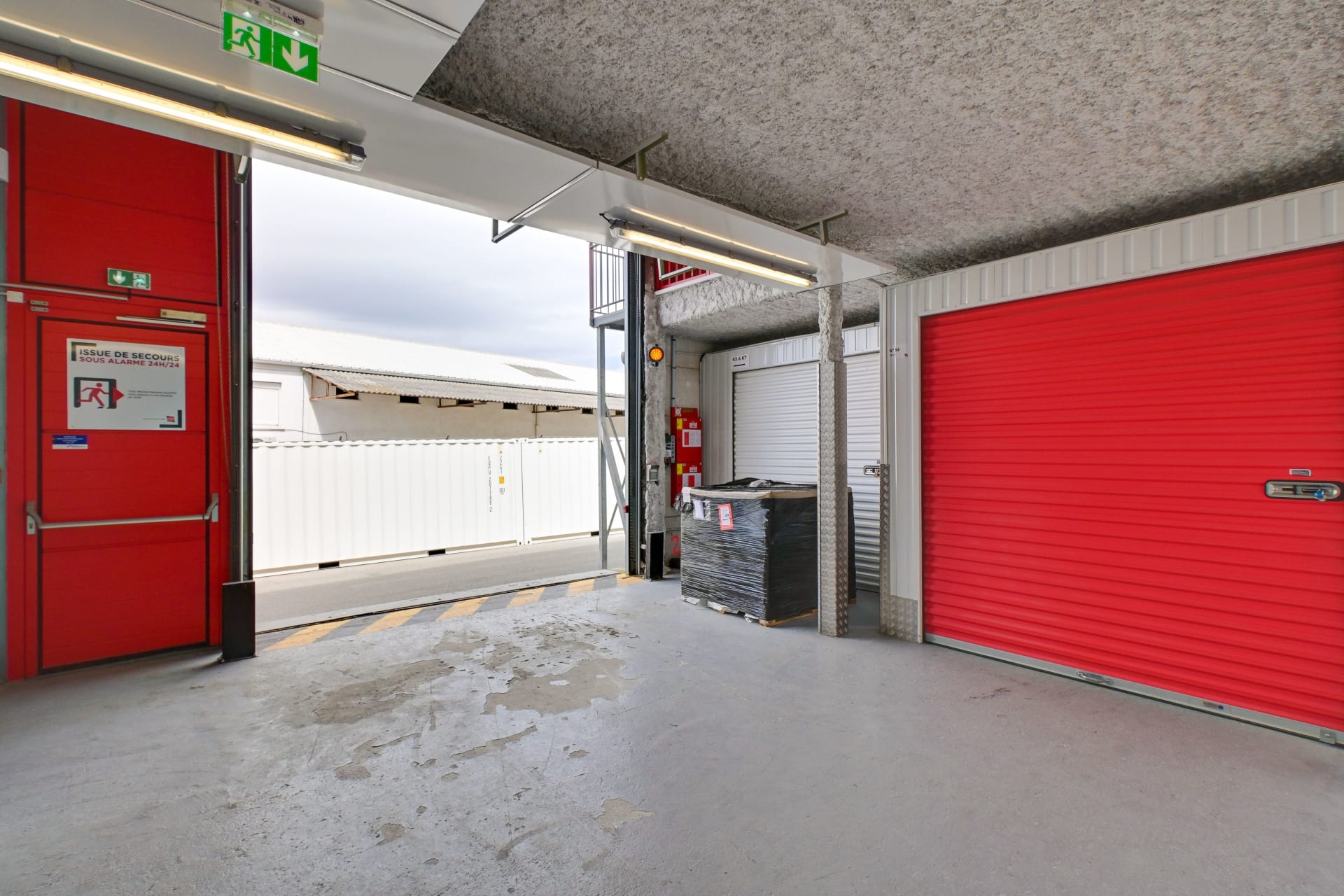 Sas intérieur avec porte d'issue de secours et rideau métallique rouge d'un box du centre HOMEBOX Les Pennes-Mirabeau