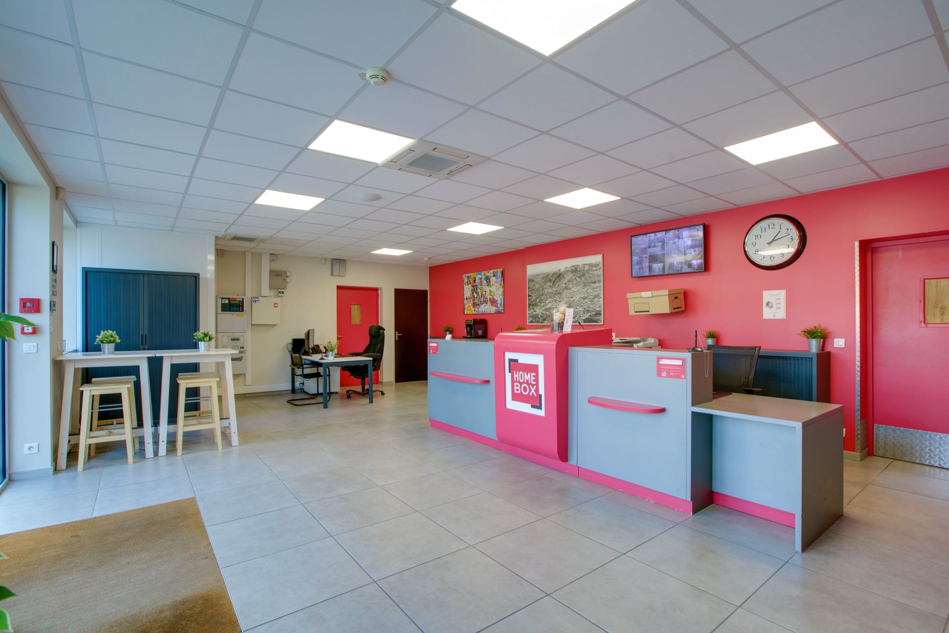 Comptoir d’accueil et espace client au centre HOMEBOX Grenoble, avec tables hautes et décor aux couleurs de la marque.