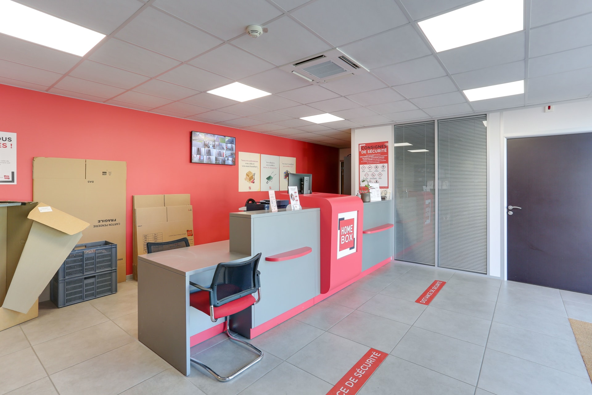 Espace d'accueil avec comptoir rose, cartons penderie et consignes de sécurité au sol du centre HOMEBOX Laval