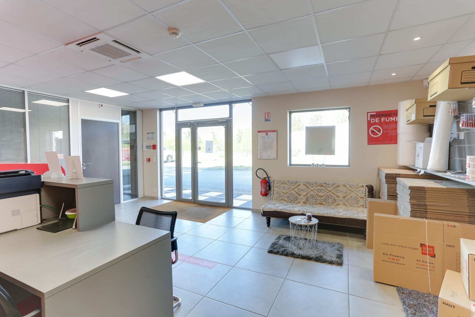 Espace d'attente avec canapé motifs, table basse et stock de cartons à plat du centre HOMEBOX Laval