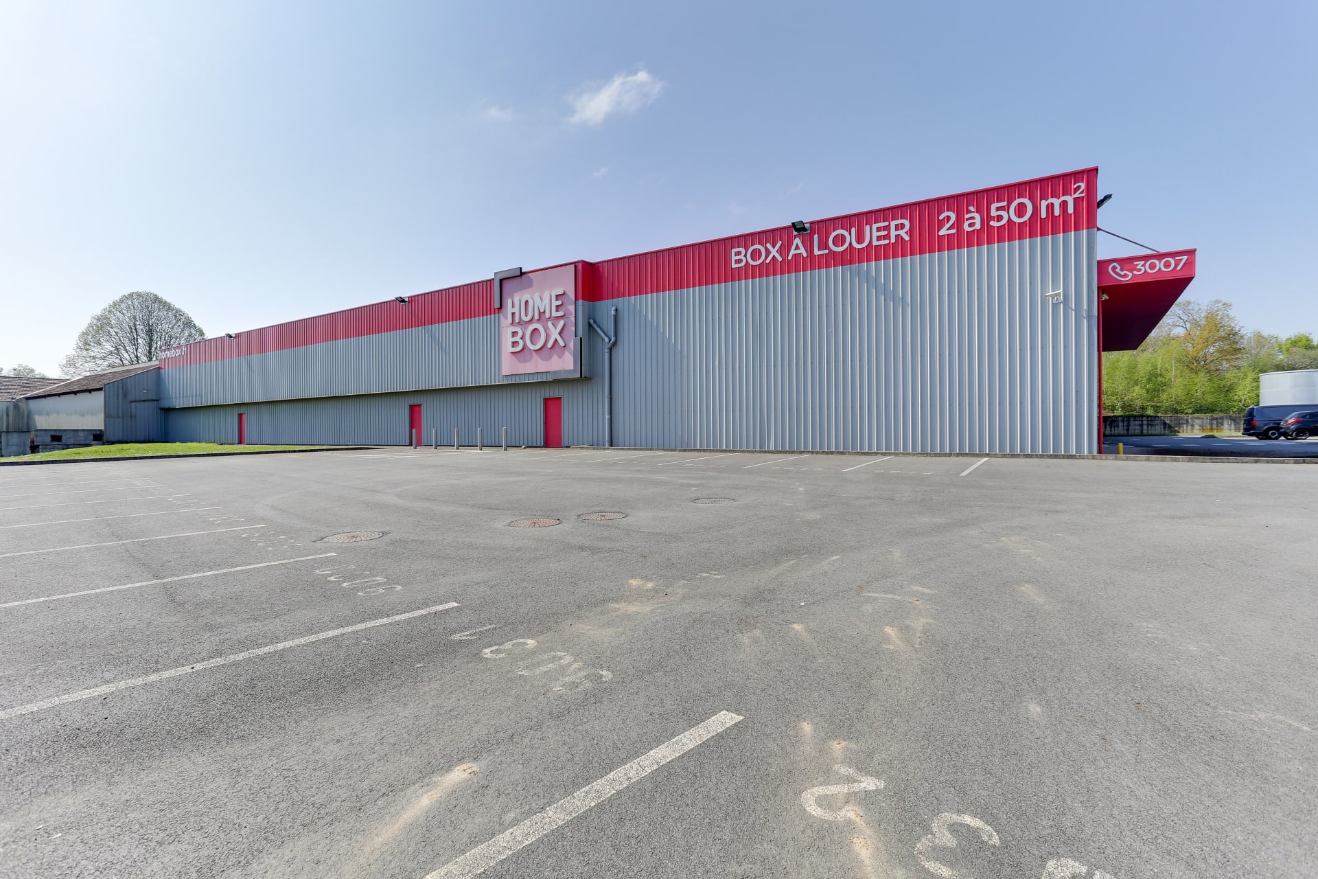 Façade latérale grise et rouge vue depuis le parking vide, HOMEBOX Laval, 19 boulevard du 8 mai 1945 à Laval