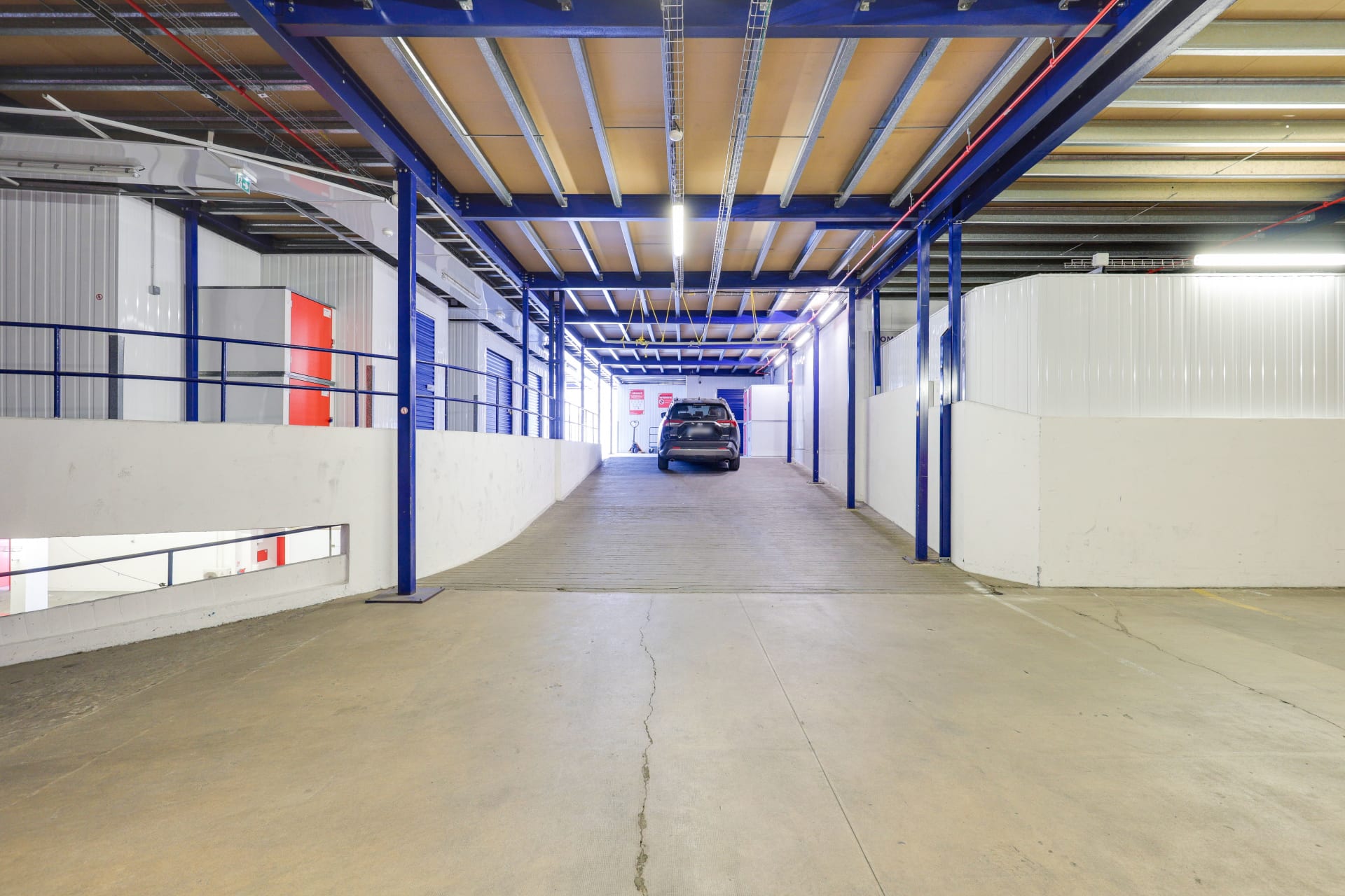 Allée de circulation intérieure avec poutres bleues menant à un véhicule en chargement du centre HOMEBOX Quimper Gare