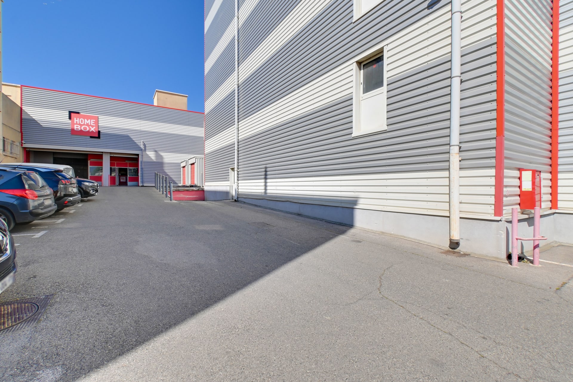 Parking ensoleillé et entrée du bâtiment au bardage gris et rouge, HOMEBOX Marseille - Littoral, 173 chemin de la Madrague-Ville à Marseille