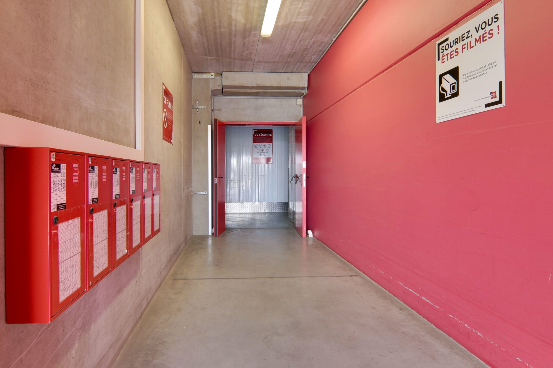 Couloir du centre HOMEBOX Avignon avec boîtes aux lettres rouges et signalétique d’ascenseur.