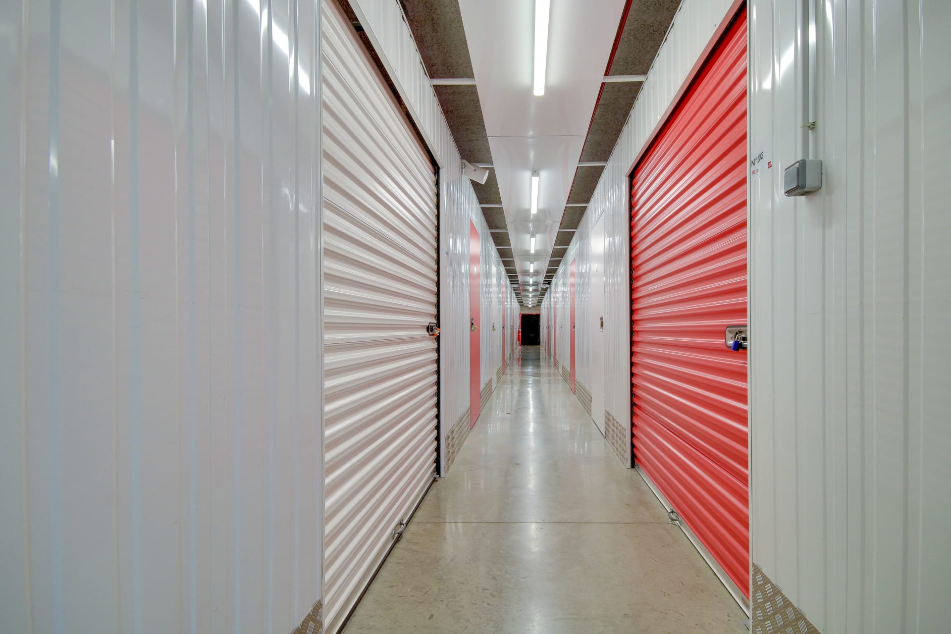 Couloir intérieur bordé de portes de box blanches et rouges en perspective du centre HOMEBOX Reims Nord