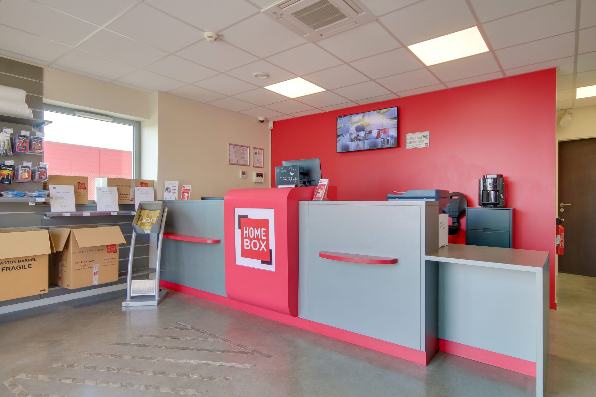 Comptoir d'accueil rose avec écran d'information et présentoirs documentaires du centre HOMEBOX Reims Nord