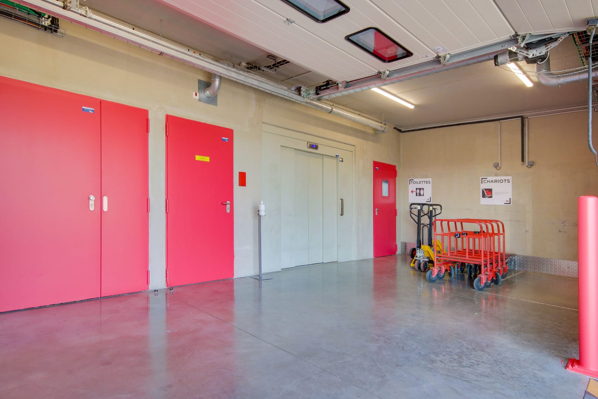 Hall intérieur avec portes coupe-feu roses, ascenseur et chariots de manutention du centre HOMEBOX Reims Nord
