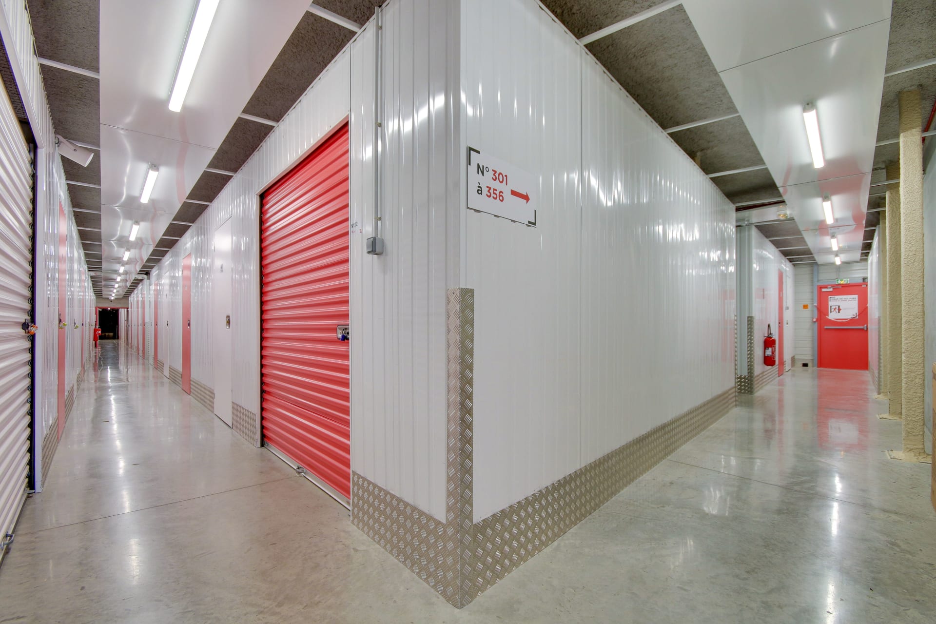 Couloir avec porte de box rouge et signalétique directionnelle vers les numéros 301 à 356 du centre HOMEBOX Reims Nord