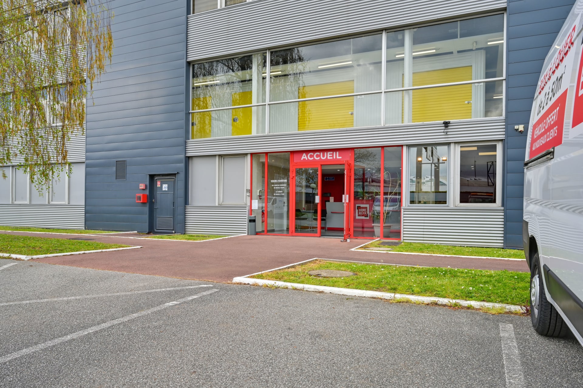 Entrée accueil rouge du bâtiment avec camionnette utilitaire stationnée, HOMEBOX Plaisir, 15 rue Descartes à Plaisir
