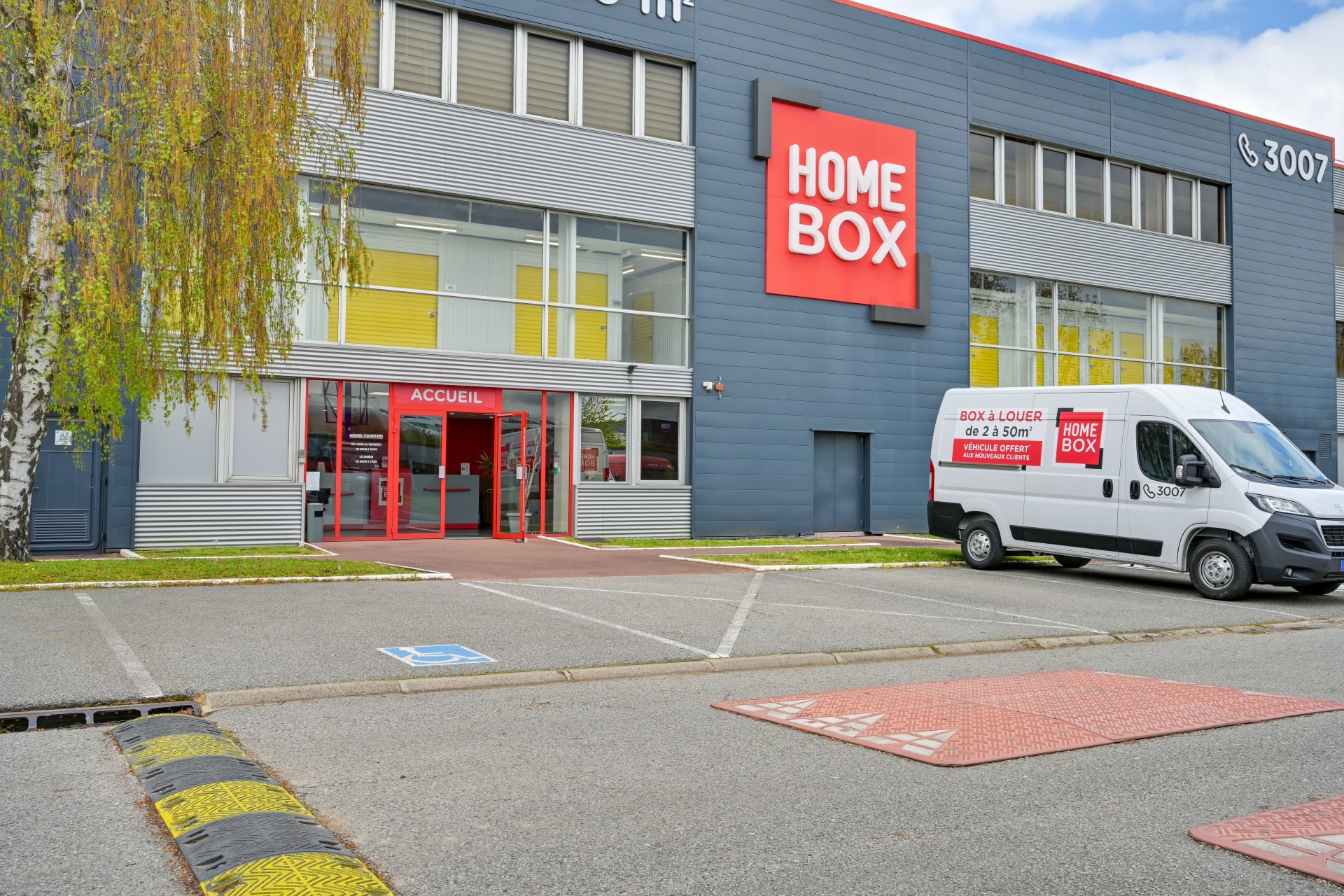 Façade du centre avec enseigne HOMEBOX, entrée accueil rouge et camionnette utilitaire, HOMEBOX Plaisir, 15 rue Descartes à Plaisir