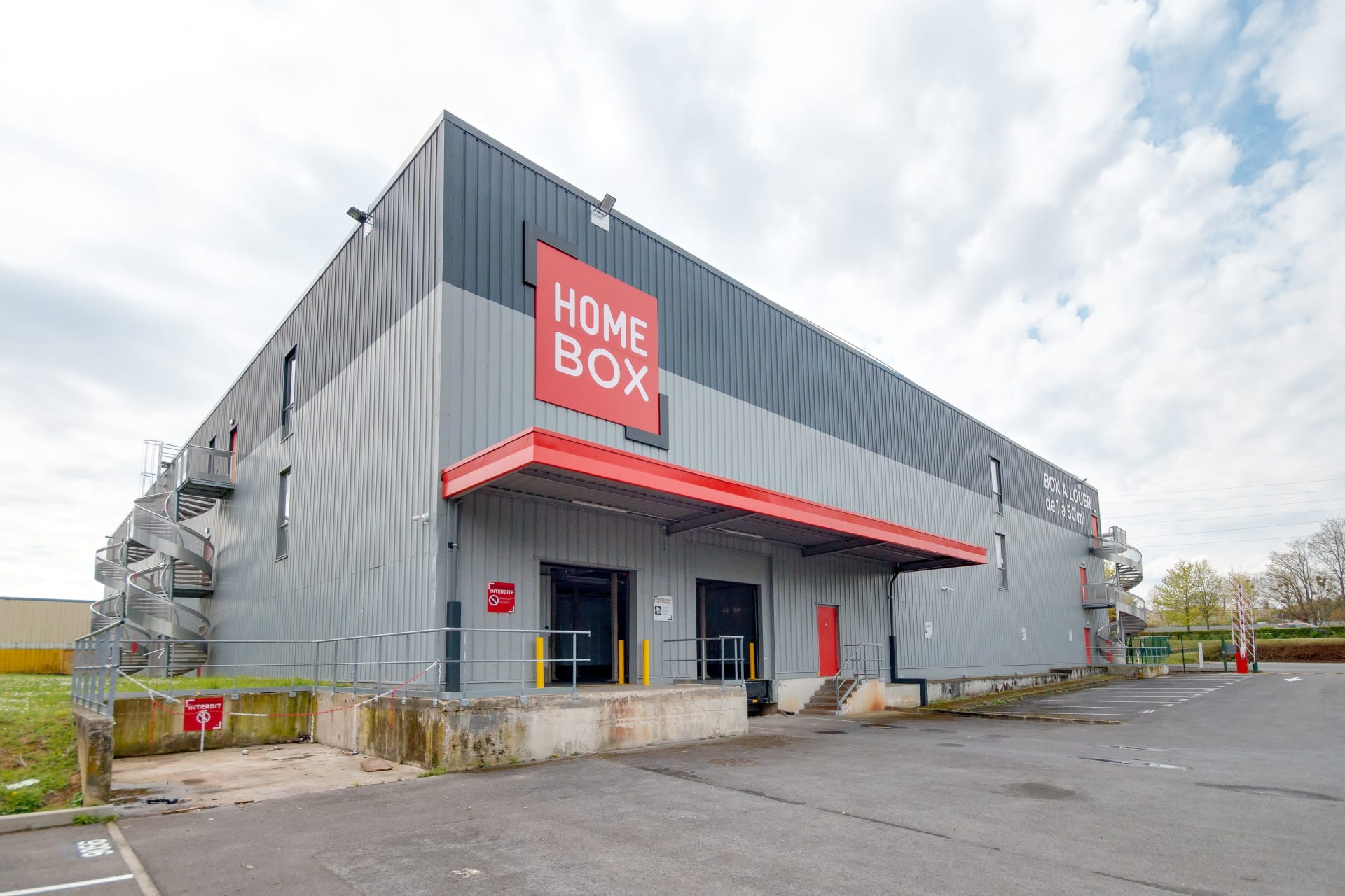 Façade d'angle gris et rouge avec enseigne HOMEBOX et auvent d'entrée, HOMEBOX Reims Sud, Rue William Shakespeare à Reims