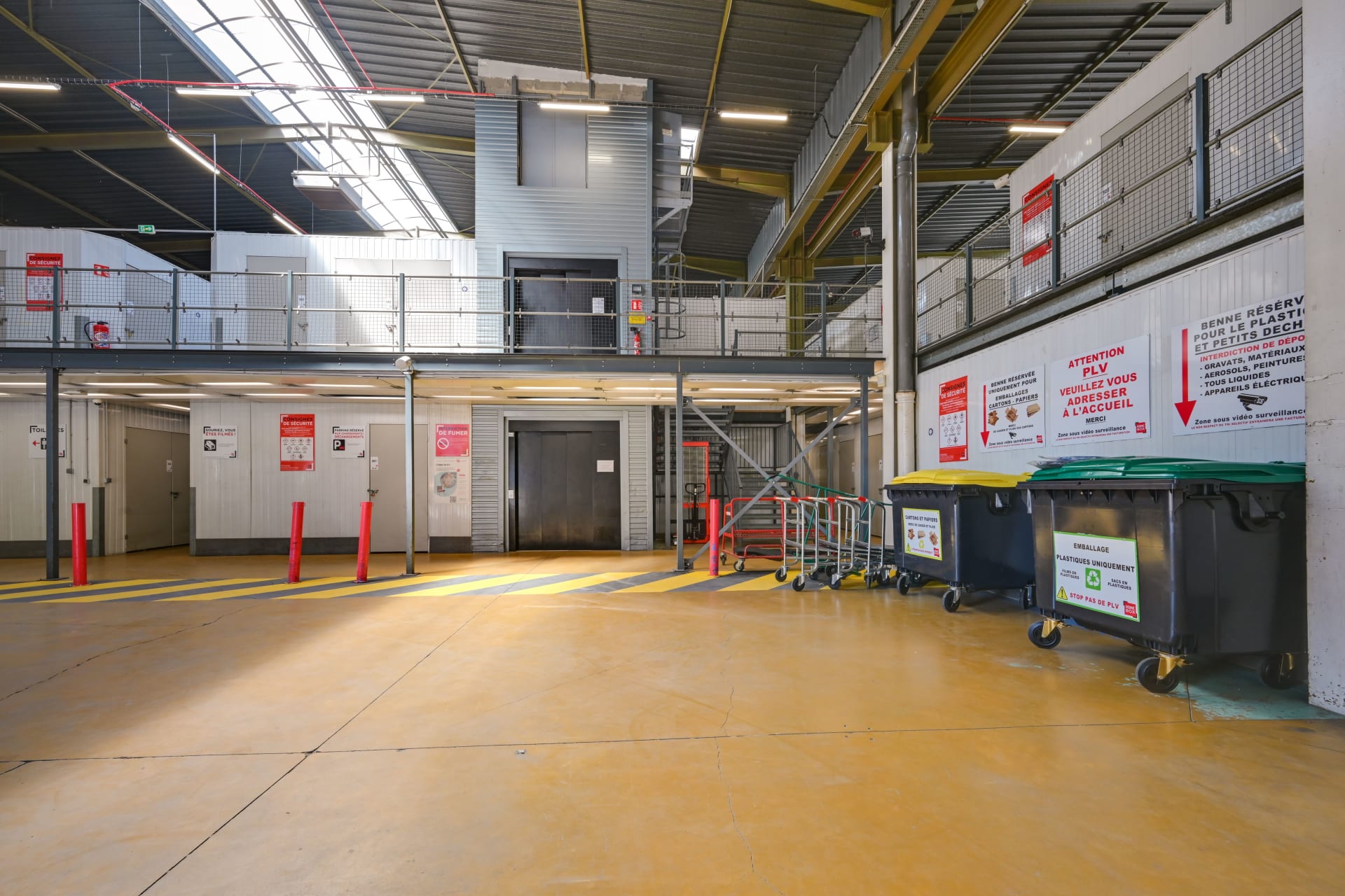 Vue latérale de la zone intérieure du centre HOMEBOX Bagnolet avec bacs de recyclage et accès à l’ascenseur.