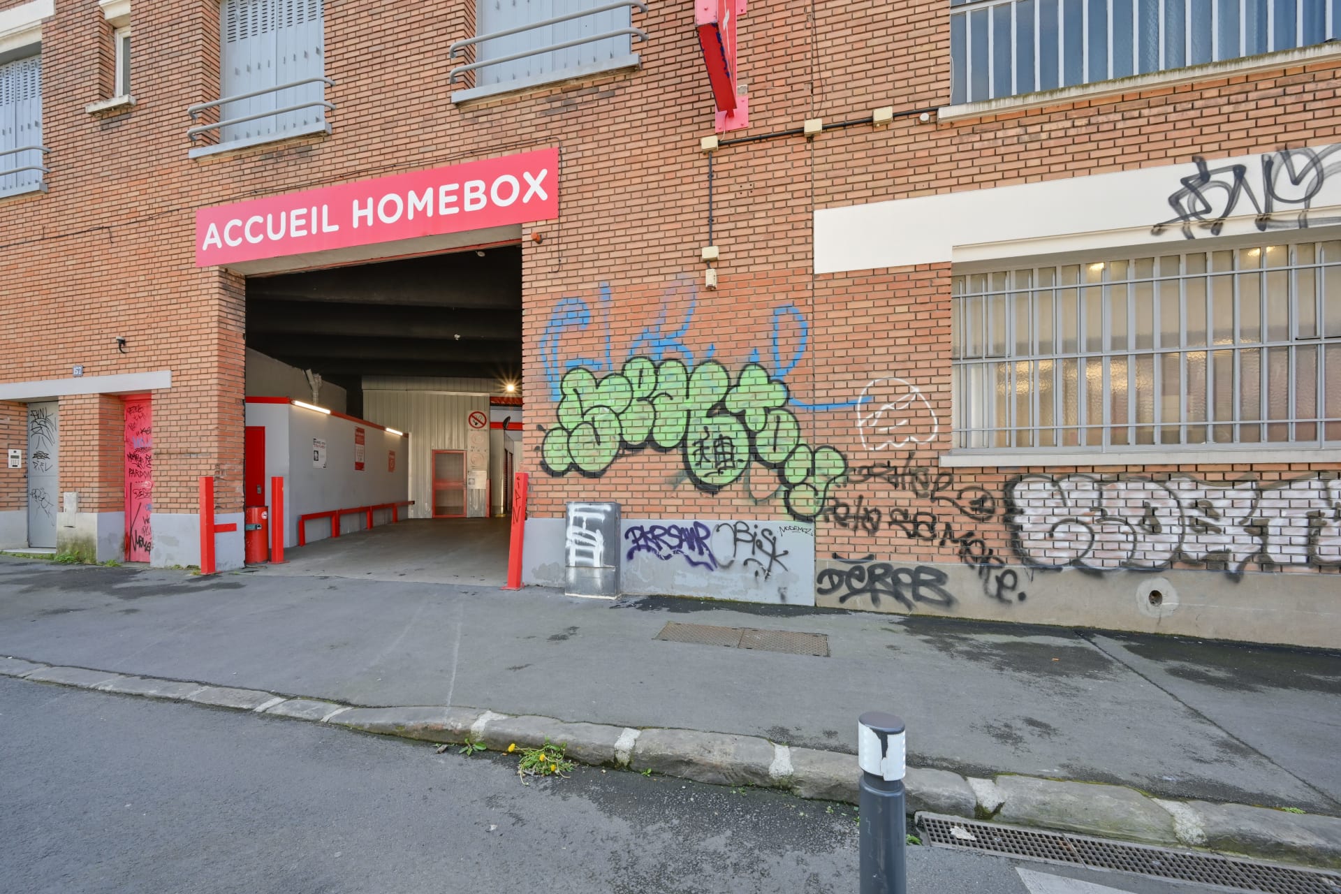 Entrée du centre sous porche avec enseigne Accueil HOMEBOX et façade en briques tagguée, HOMEBOX Montreuil, 157 boulevard de Chanzy à Montreuil
