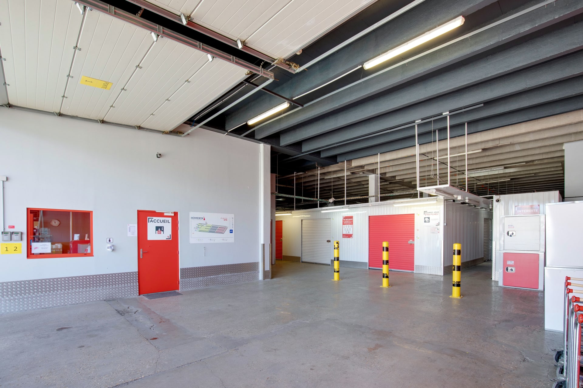 Zone de chargement intérieure avec boxes rouges, plots de sécurité jaunes et porte d'accueil du centre HOMEBOX Le Havre