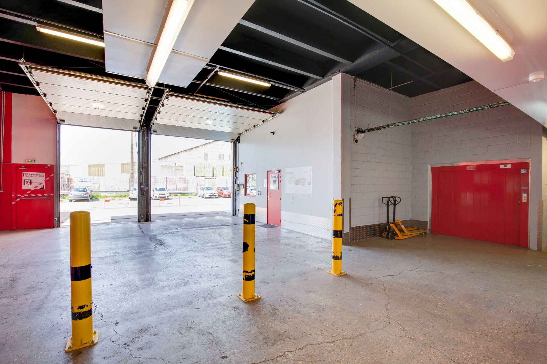 Zone de chargement intérieure avec porte sectionnelle ouverte sur le parking, plots jaunes et transpalette du centre HOMEBOX Le Havre