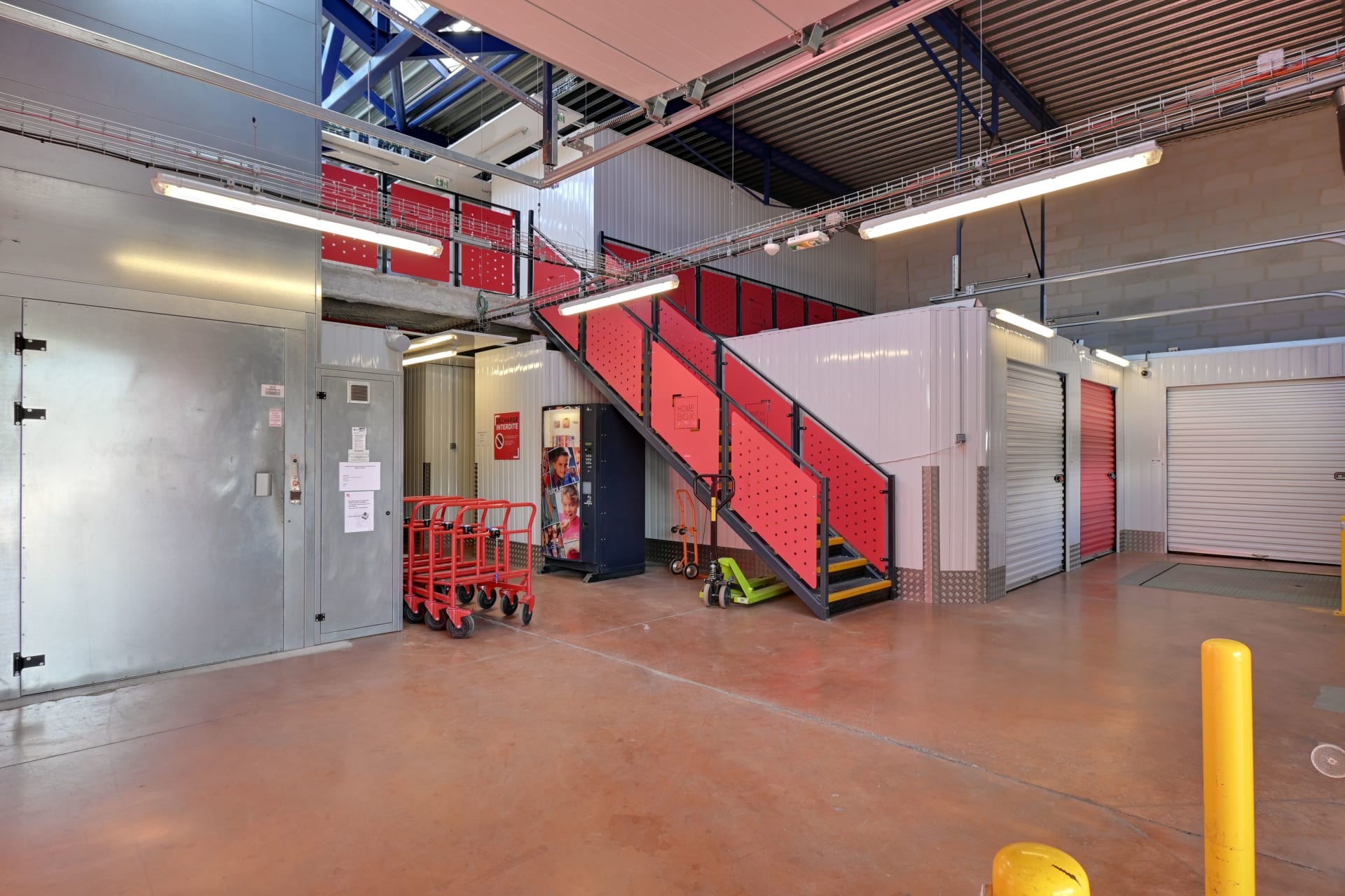 Hall intérieur avec escalier rouge, chariots de manutention et portes de boxes alignées du centre HOMEBOX Toulon - La Farlède