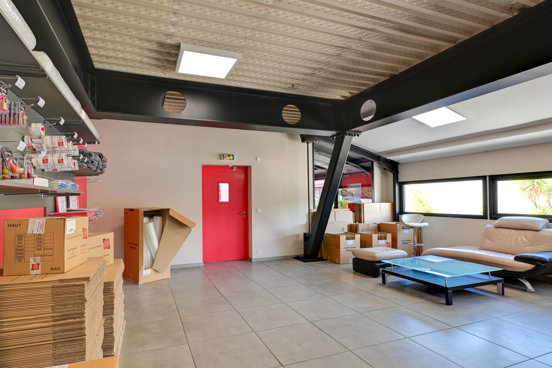 Espace boutique avec rayonnages de fournitures, porte rouge et coin salon vitré du centre HOMEBOX Toulon - La Farlède