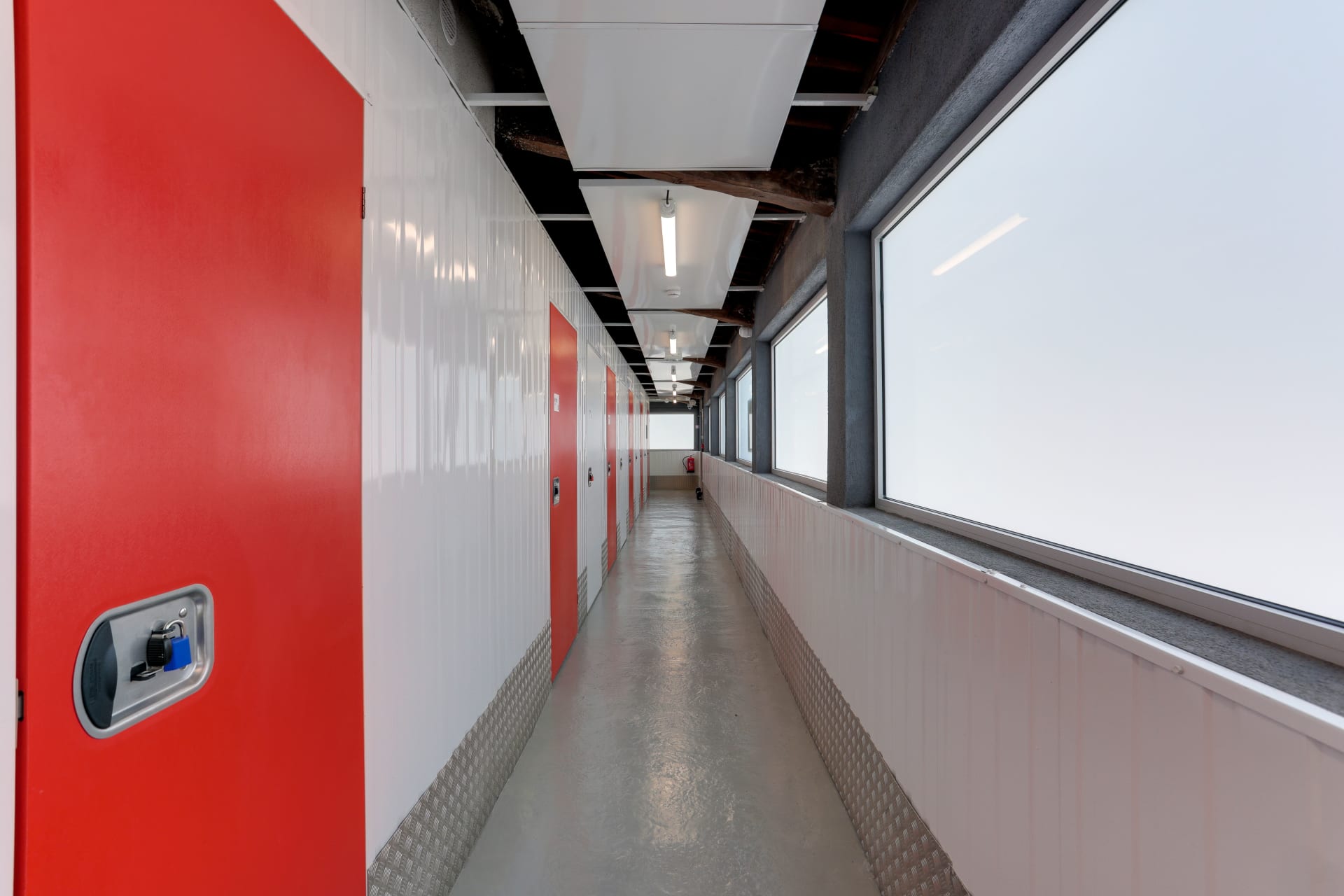 Long couloir lumineux bordé de box blancs et portes rouges du centre HOMEBOX Nice-Carros