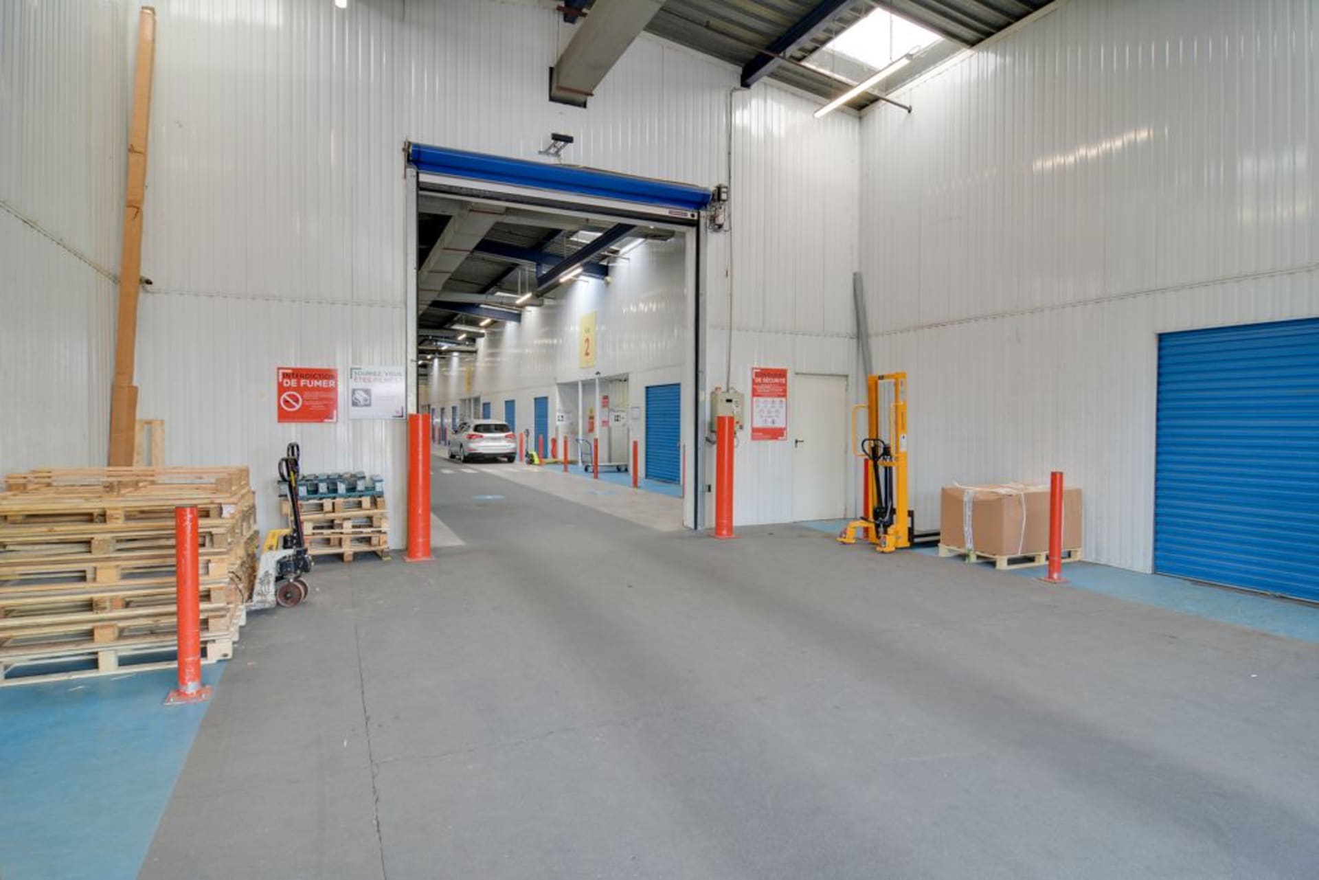 Zone de déchargement avec porte rideau bleue, palettes en bois et transpalettes du centre HOMEBOX Nantes