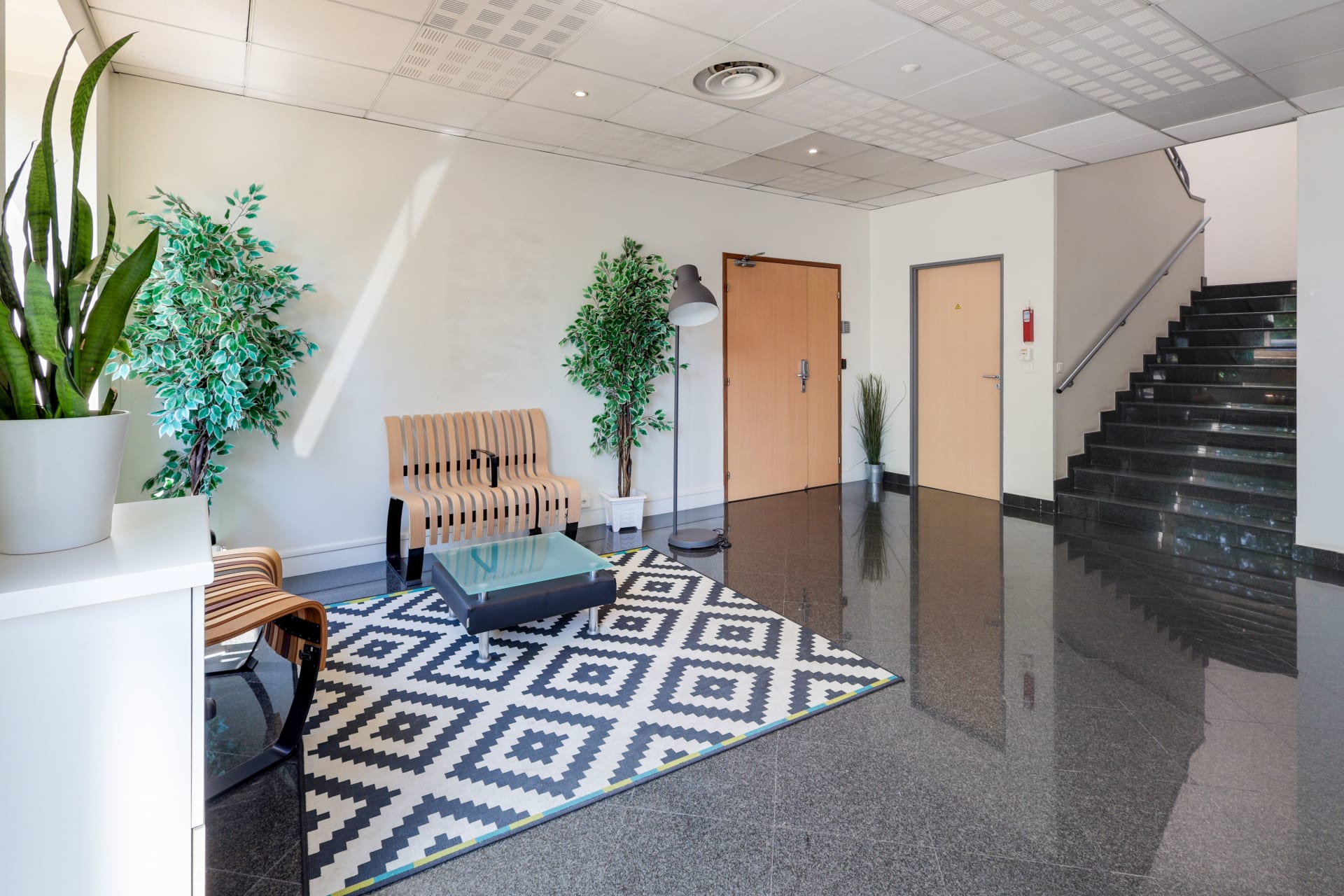 Hall d'entrée avec banc en bois, plantes vertes, tapis graphique et escalier en marbre du centre HOMEBOX Roissy