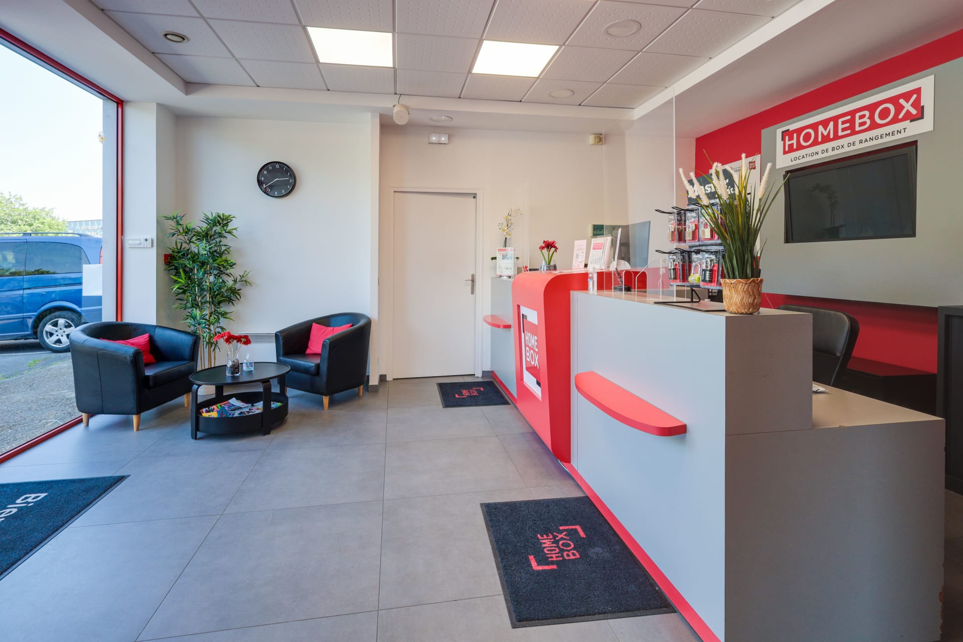 Espace d'accueil avec fauteuils noirs, baie vitrée et comptoir signé du centre HOMEBOX Roissy