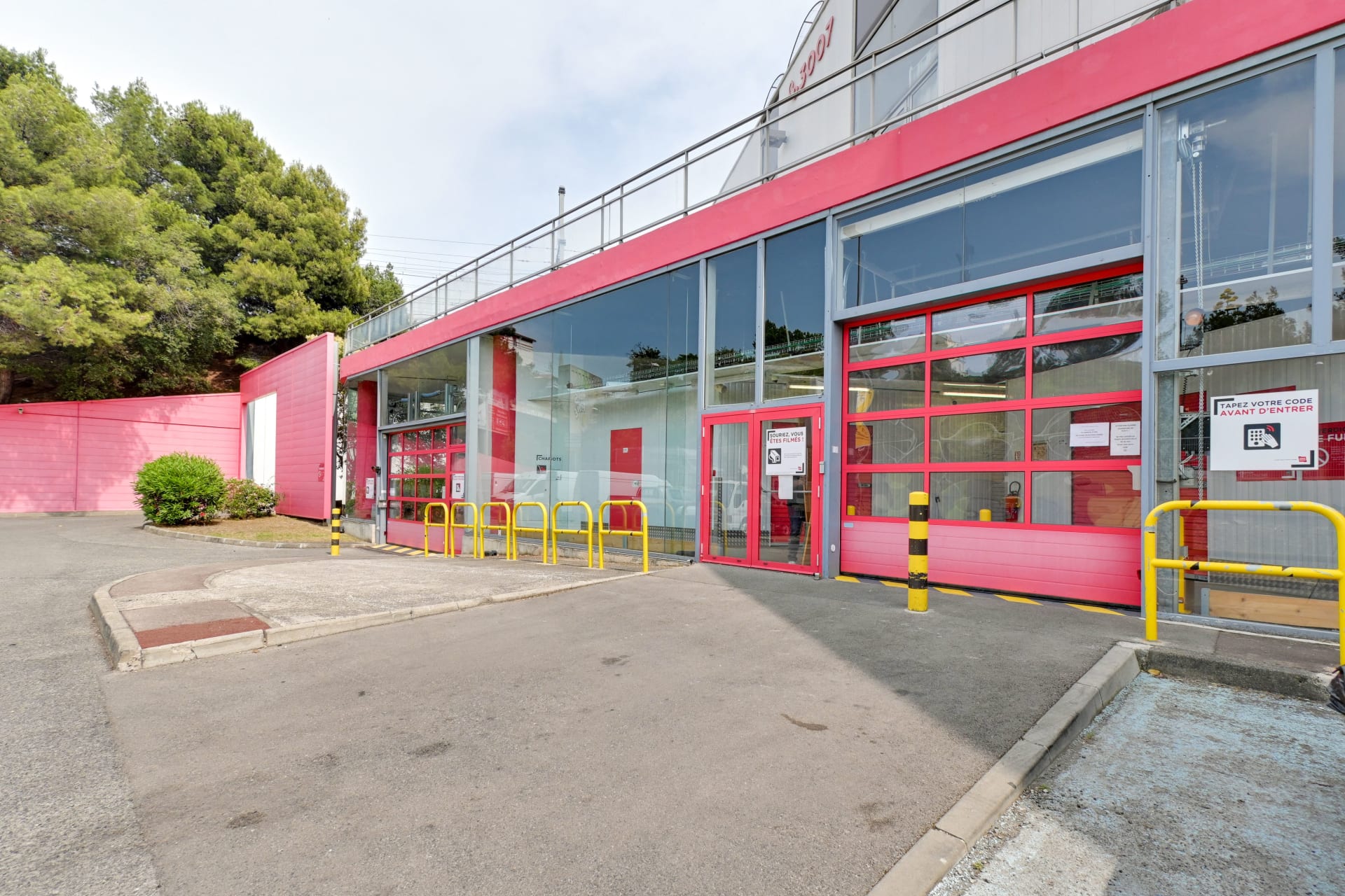 Façade vitrée rose avec porte sectionnelle et barrières jaunes de protection, HOMEBOX Marseille - Plombières, 43 Boulevard Guigou à Marseille