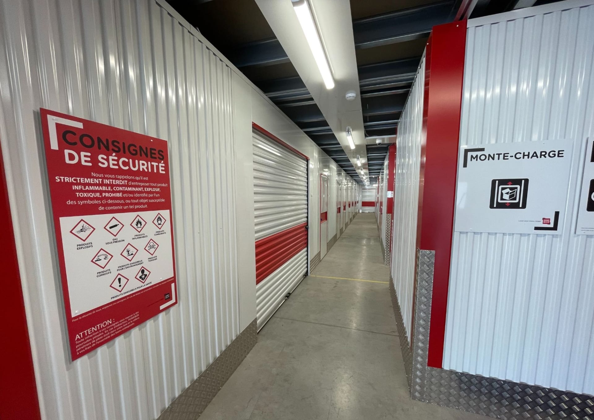 Couloir intérieur du centre HOMEBOX Albertville avec panneaux de sécurité et box de stockage.