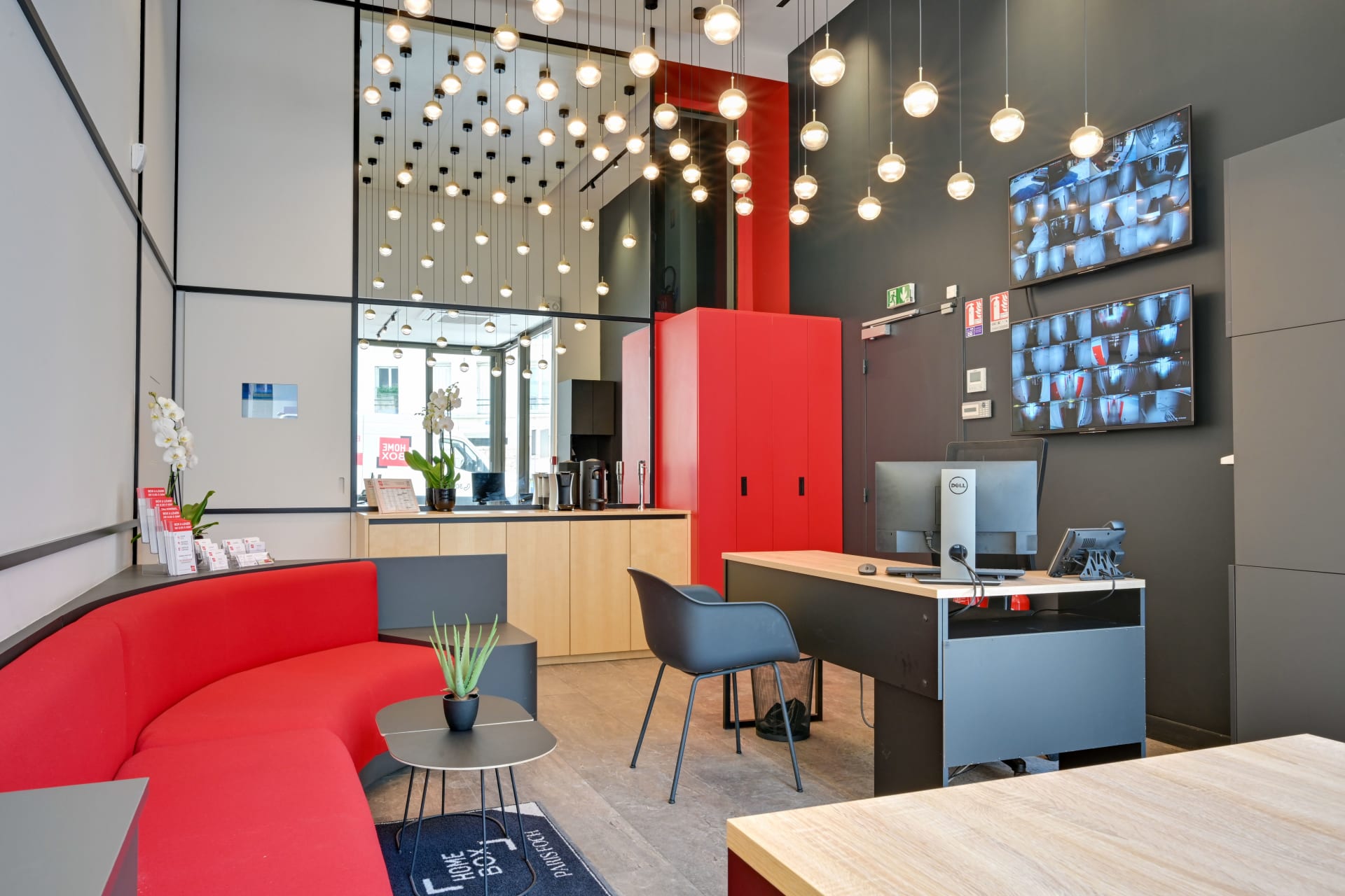 Espace d'accueil design avec banquette rouge, suspensions lumineuses et écrans de vidéosurveillance du centre HOMEBOX Paris 16