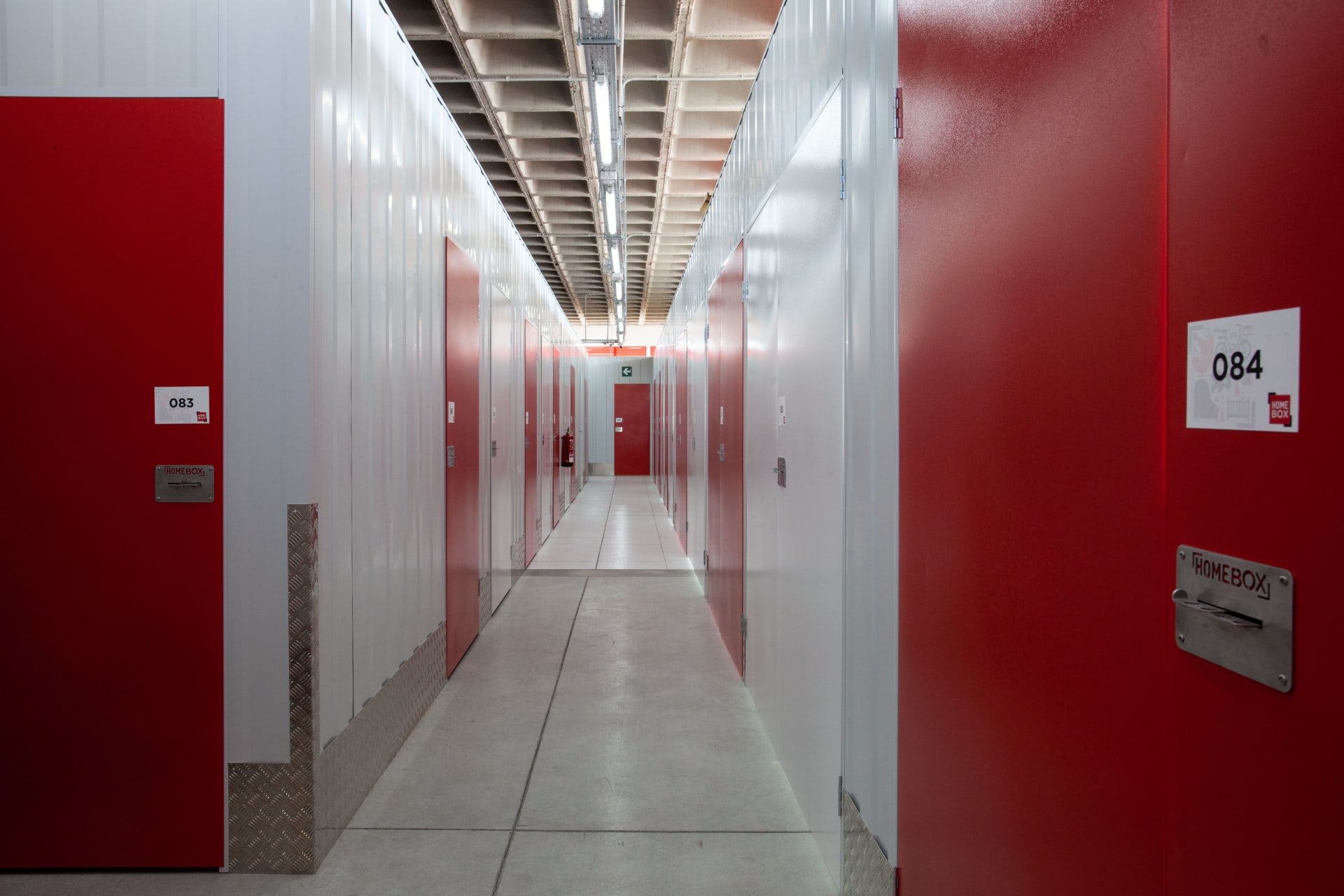 Indoor corridor with numbered red storage unit doors and polished concrete floor at HOMEBOX Girona