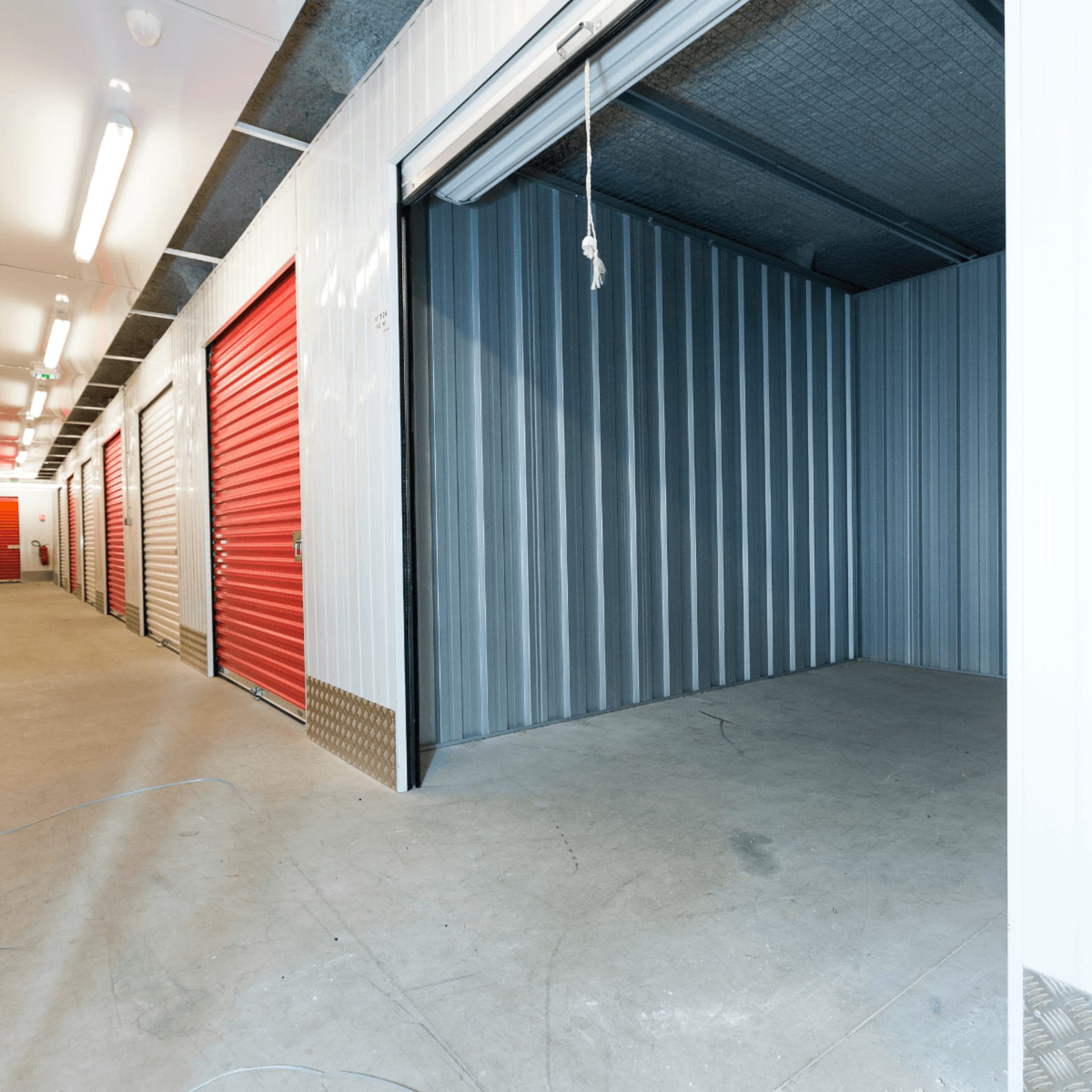 Indoor storage unit with open grey rolling door and red doors along corridor at HOMEBOX Carabanchel