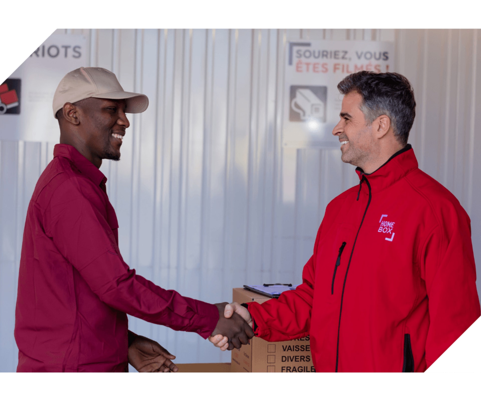 Deux collaborateurs HOMEBOX en uniforme rouge échangeant une poignée de main devant des cartons de stockage