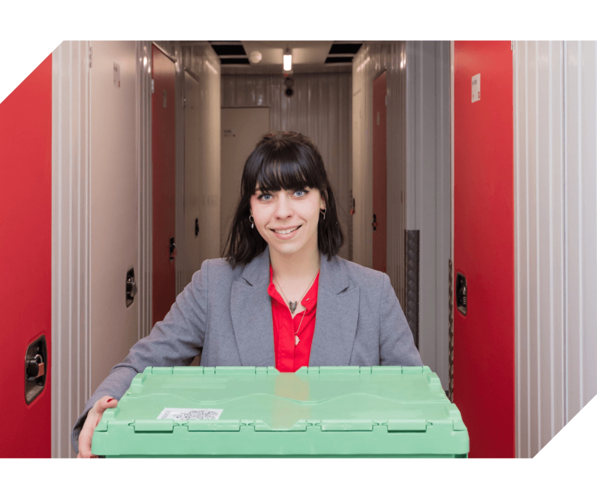 Conseillère HOMEBOX souriante tenant une boîte consignée verte dans un couloir éclairé de boxes de stockage