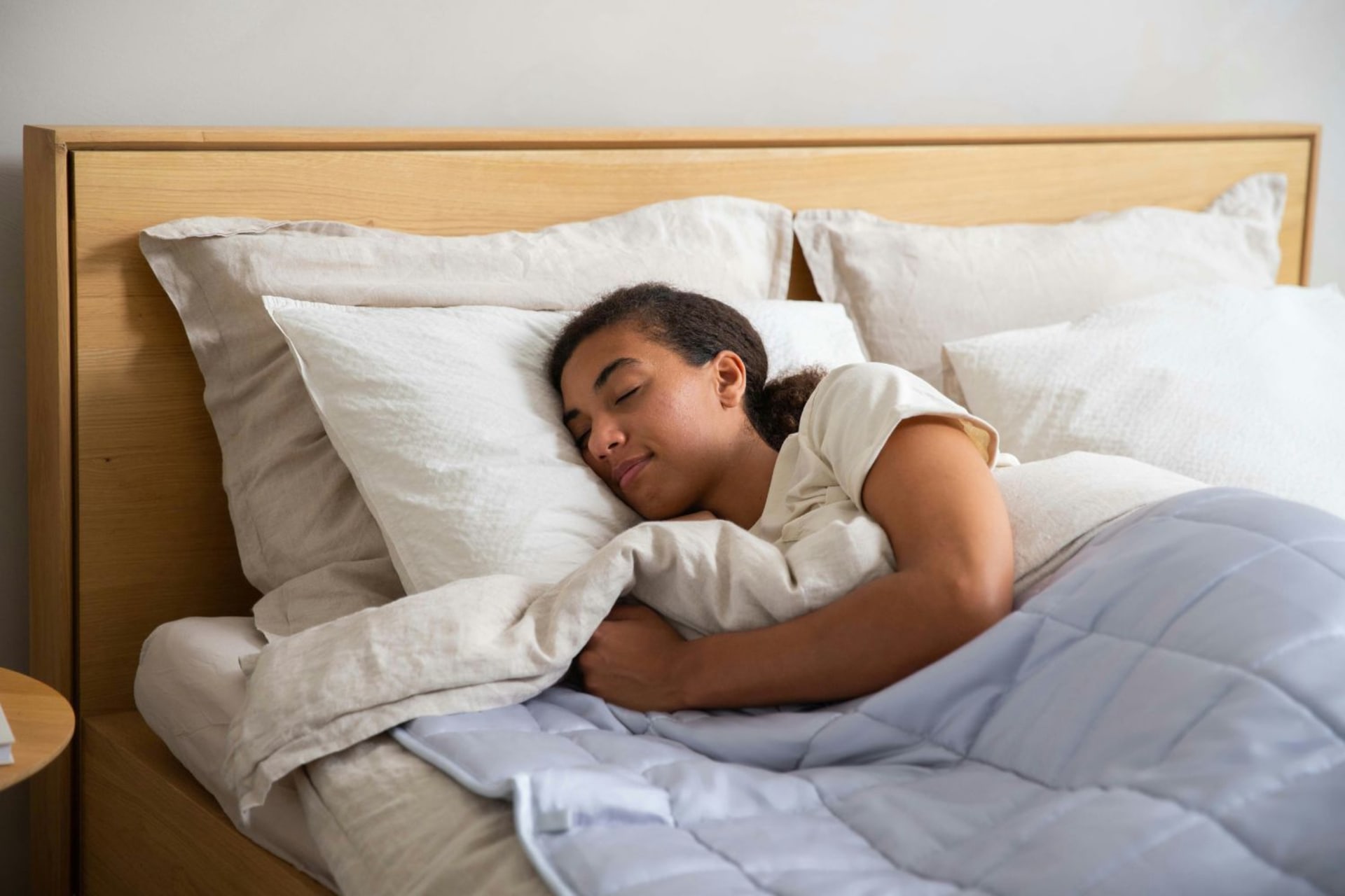 Personne dormant dans un lit deux places avec une literie blanche et une petite couette bleu lila
