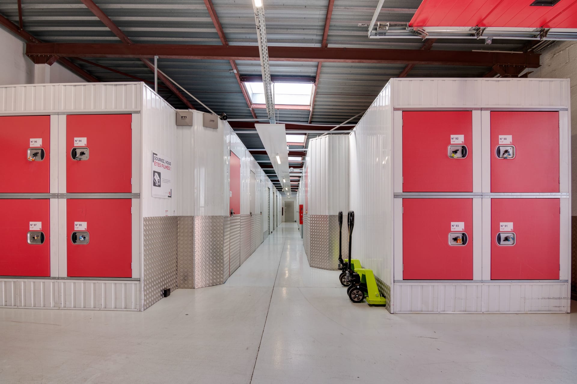 Couloir intérieur avec boxes blancs à portes rouges sur deux niveaux et transpalette du centre HOMEBOX Montpellier