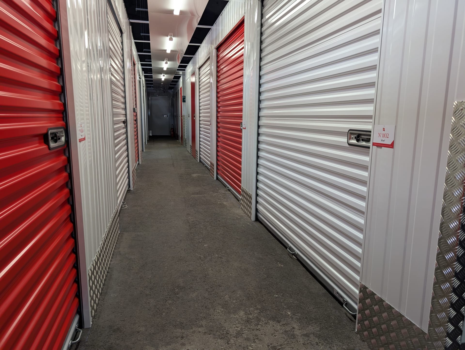 Couloir intérieur avec rangées de portes de boxes rouges et blancs et tôle striée du centre HOMEBOX Dunkerque