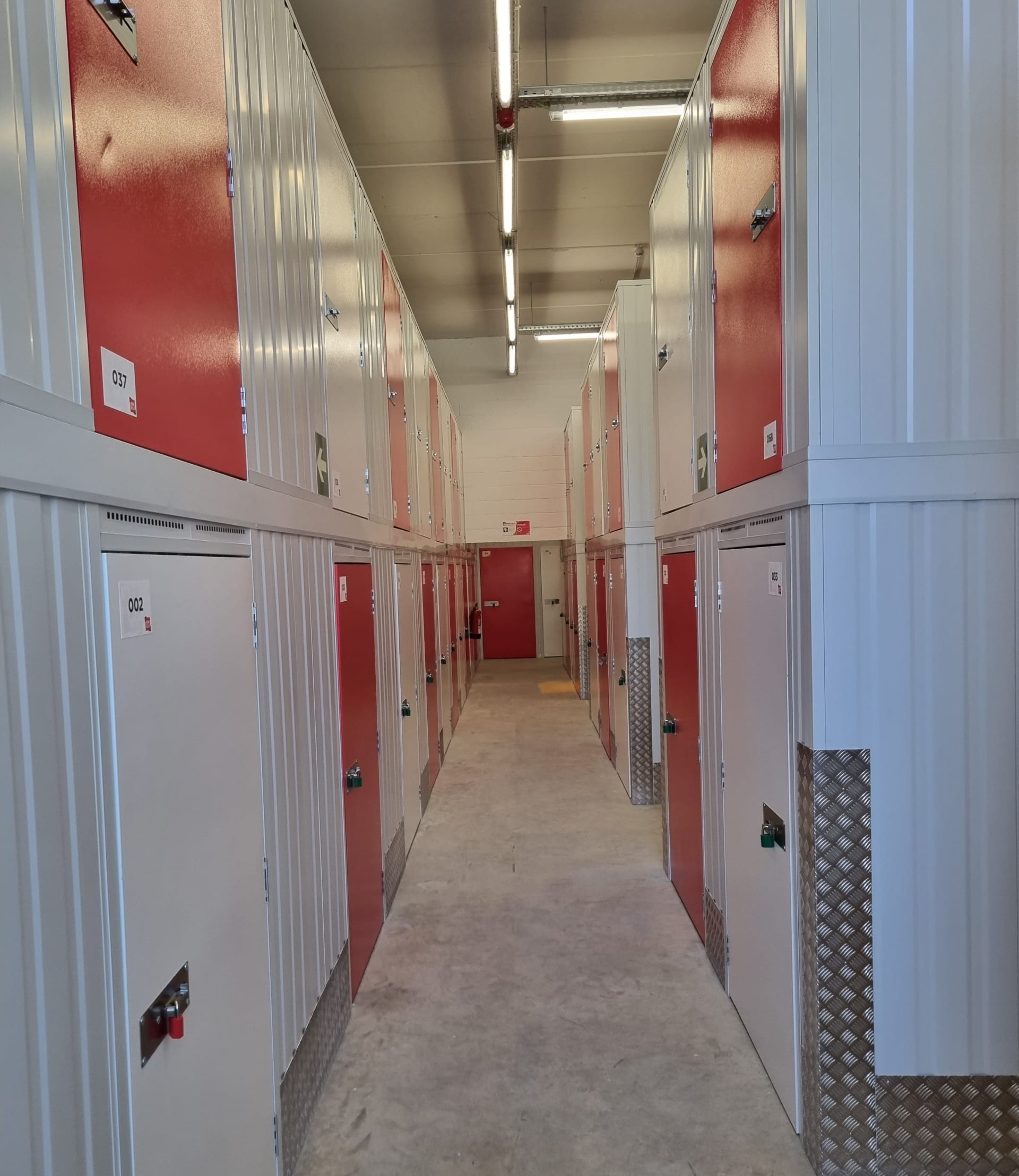 Long indoor aisle with red storage doors on white walls under fluorescent lighting at HOMEBOX Blanes