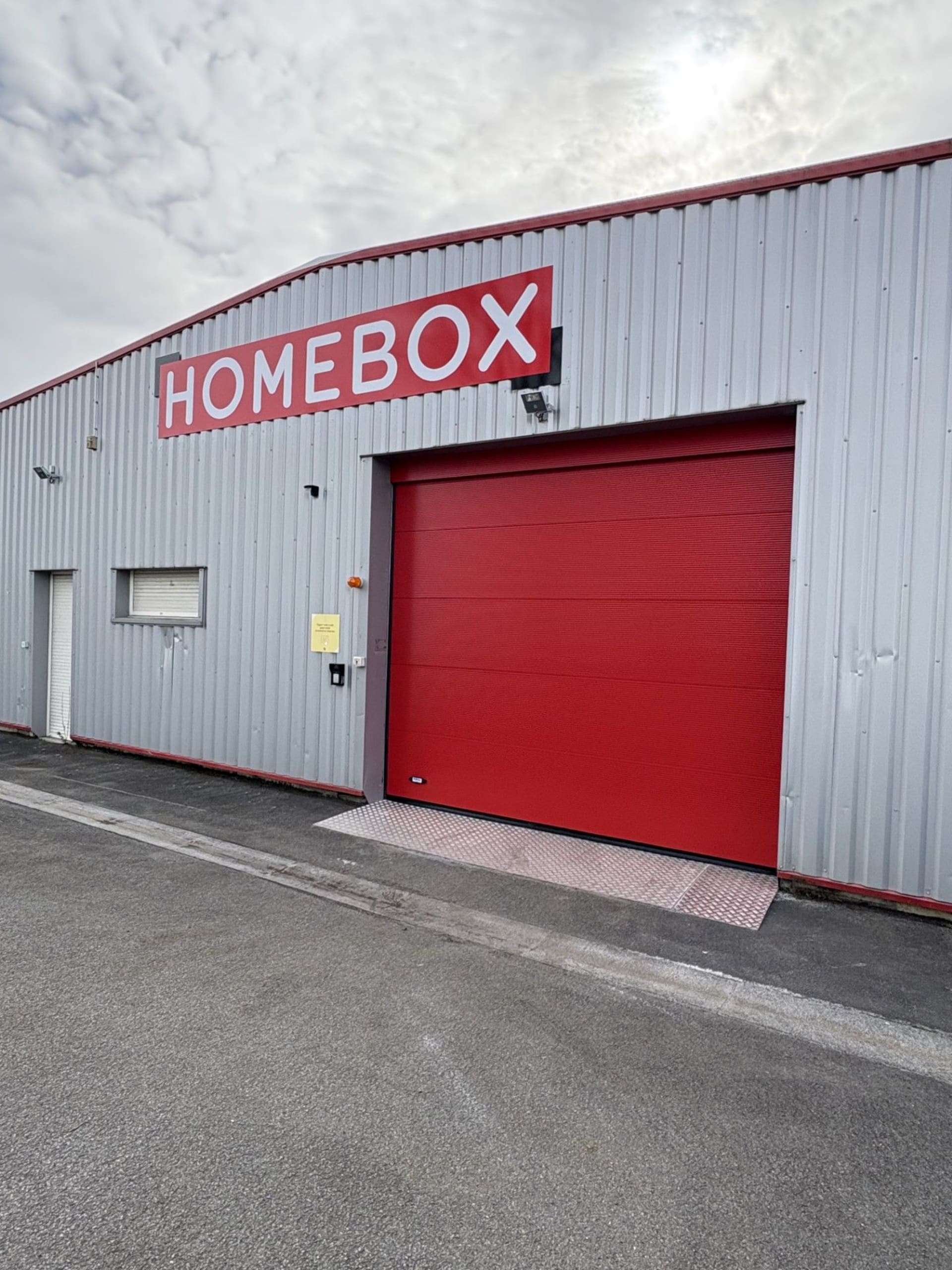 Façade grise avec enseigne rouge HOMEBOX et porte de quai de chargement, HOMEBOX Angoulême La Couronne, 17 rue de la Pinotière à La Couronne