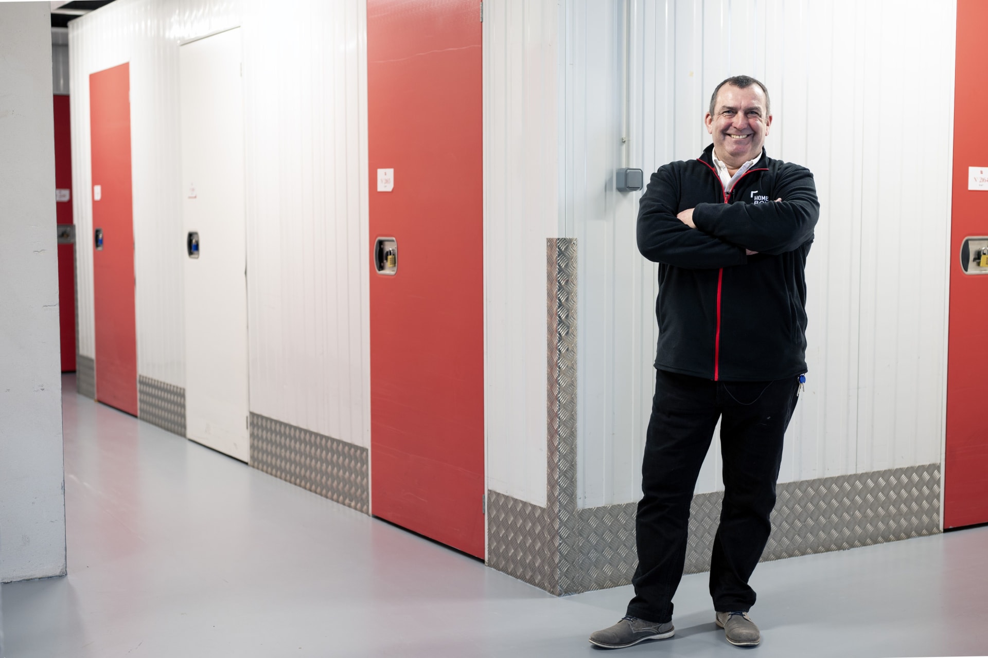 Gérant souriant en tenue HOMEBOX devant les portes rouges et blanches des boxes du centre HOMEBOX Lyon Saint-Priest